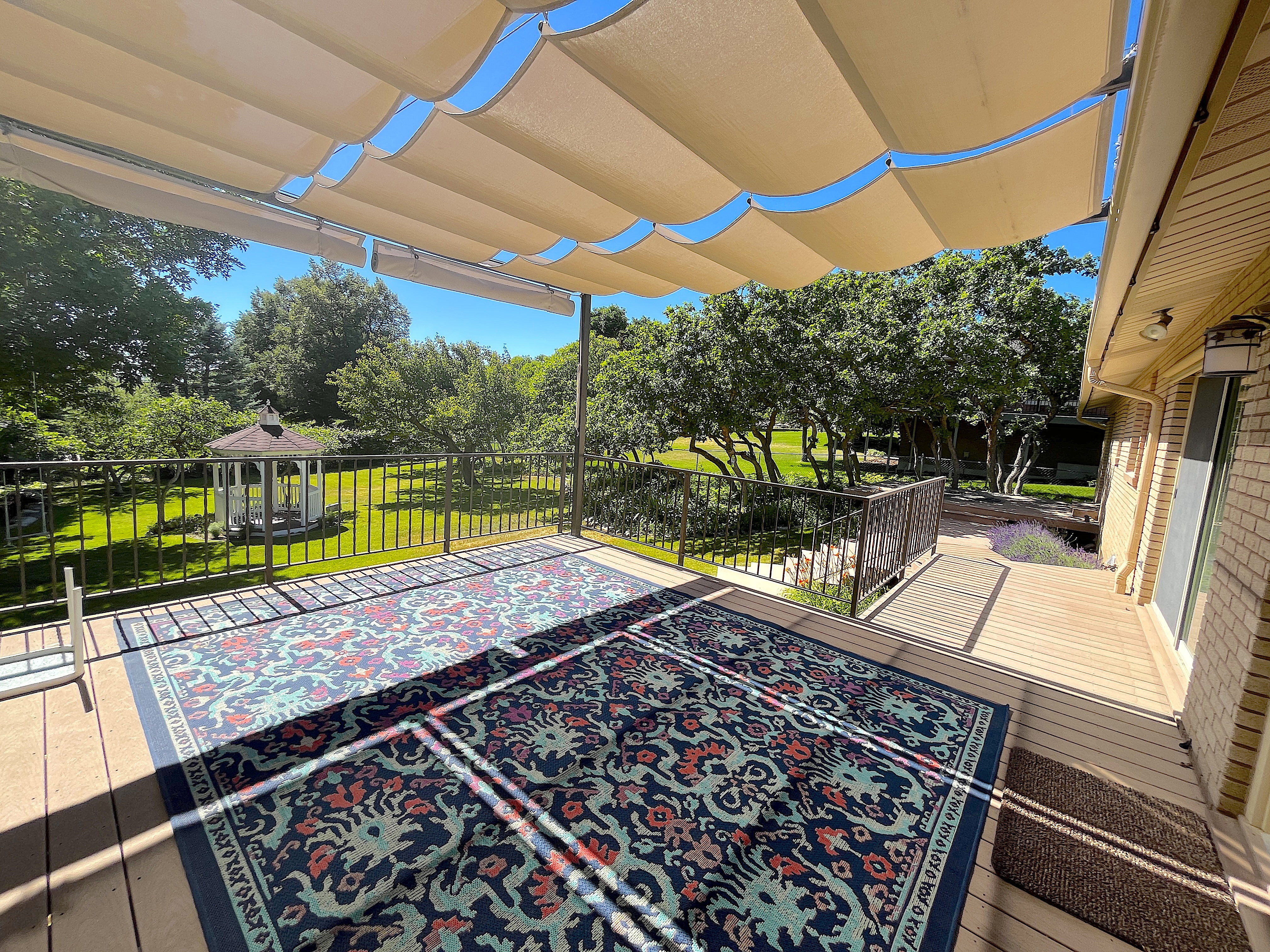 Spacious outdoor deck featuring a retractable fabric canopy, metal railings, and a wood-finish surface