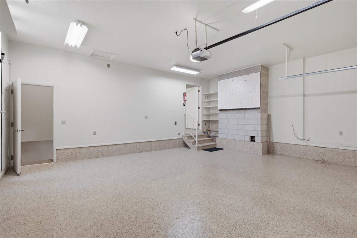 Spacious garage featuring a speckled epoxy floor, white painted walls, exposed block construction, built-in shelving, and a visible garage door opener mechanism