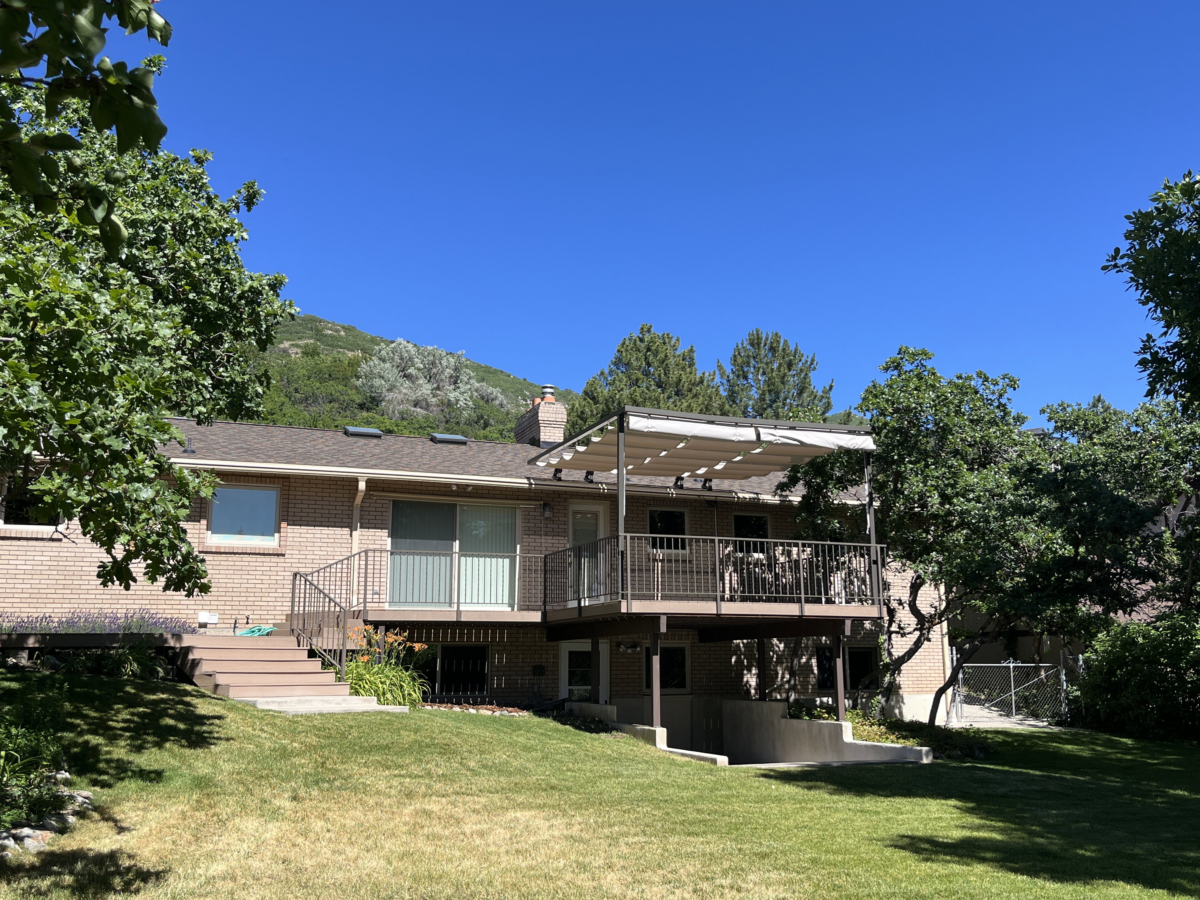 Brick exterior with an upper-level deck featuring a retractable canopy, metal railings, and a lower patio area