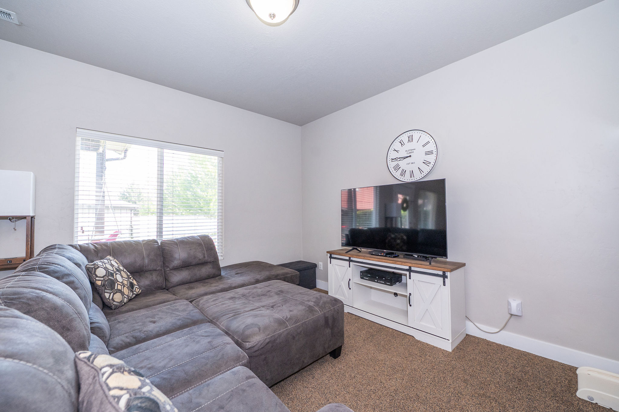 Living area featuring a large window with blinds, neutral wall paint, and a built-in entertainment console with barn door accents