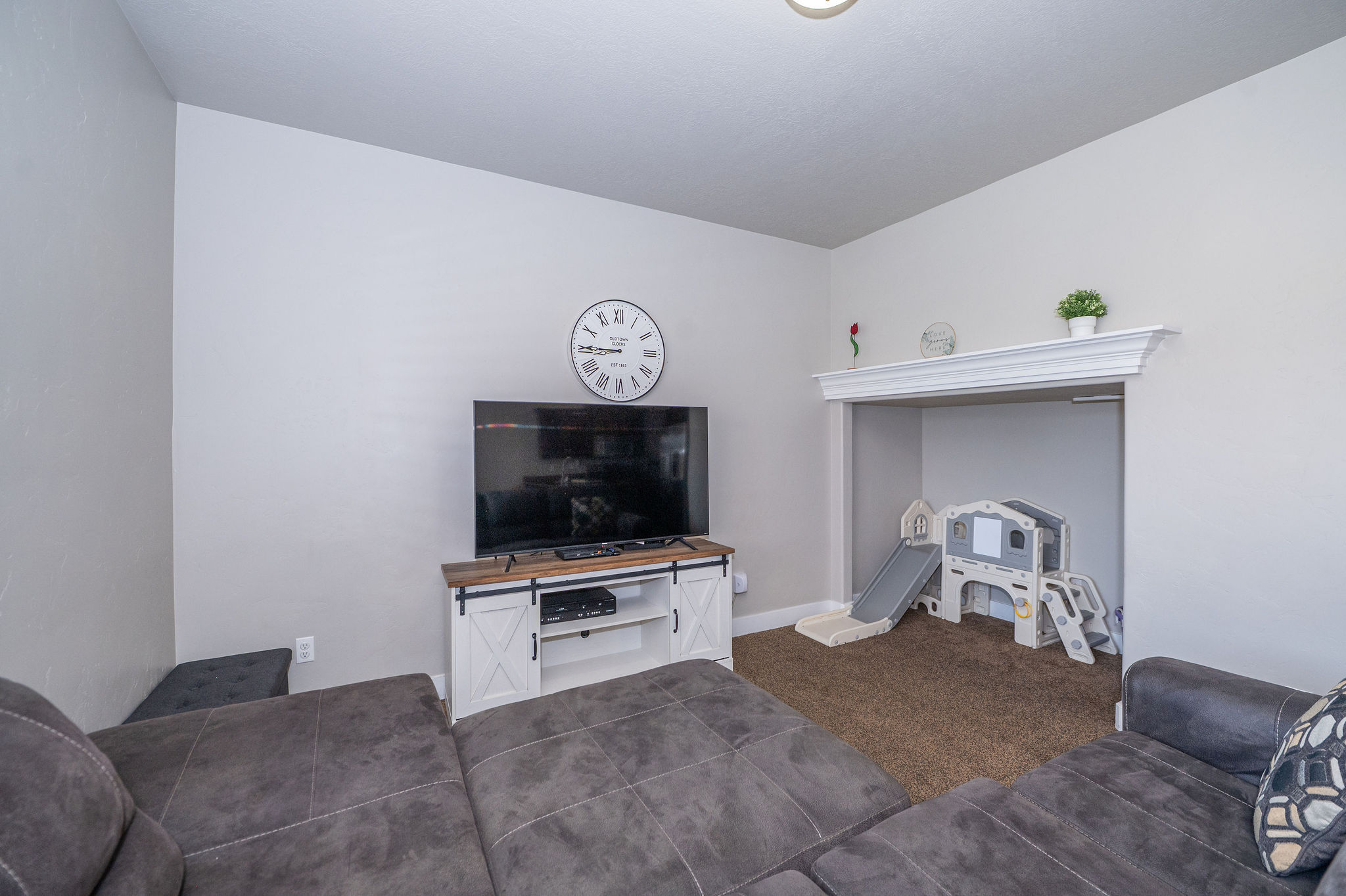 Recessed alcove with carpeted flooring and an ornate mantel, complemented by light gray wall paint and a light fixture