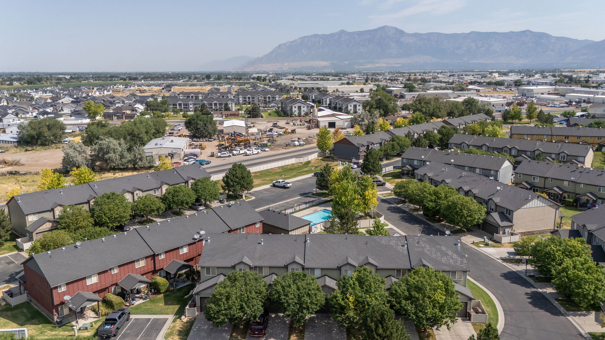 Aerial perspective showcasing a residential community with multi-story townhomes, dark shingle roofing, and mature perimeter trees