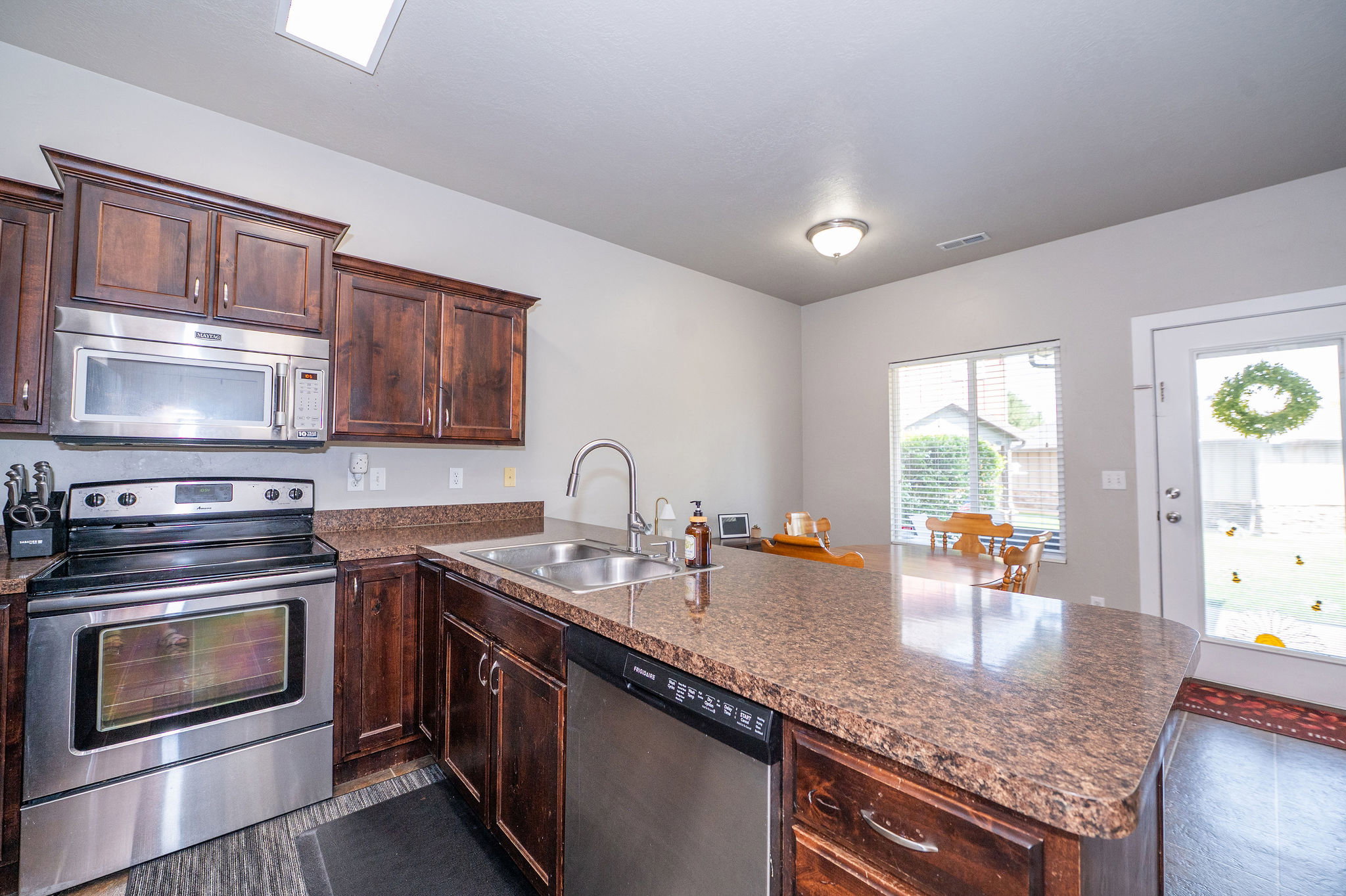 Kitchen featuring dark wood cabinetry, stainless steel appliances, a composite countertop, and an integrated kitchen island with a sink and dishwasher