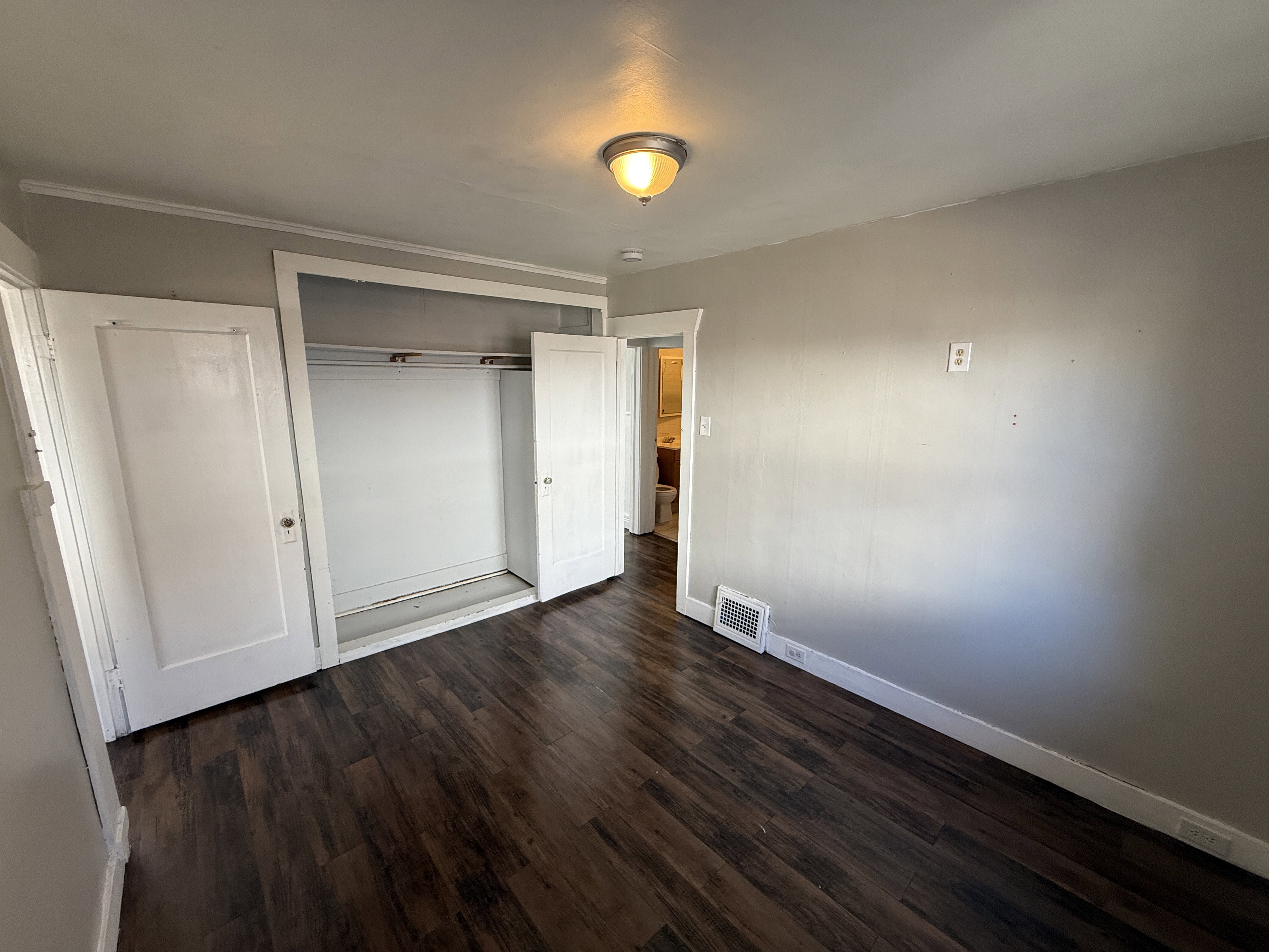 Bedroom featuring wood-finish flooring, a built-in closet with bi-fold doors, neutral wall paint, and a ceiling-mounted light fixture