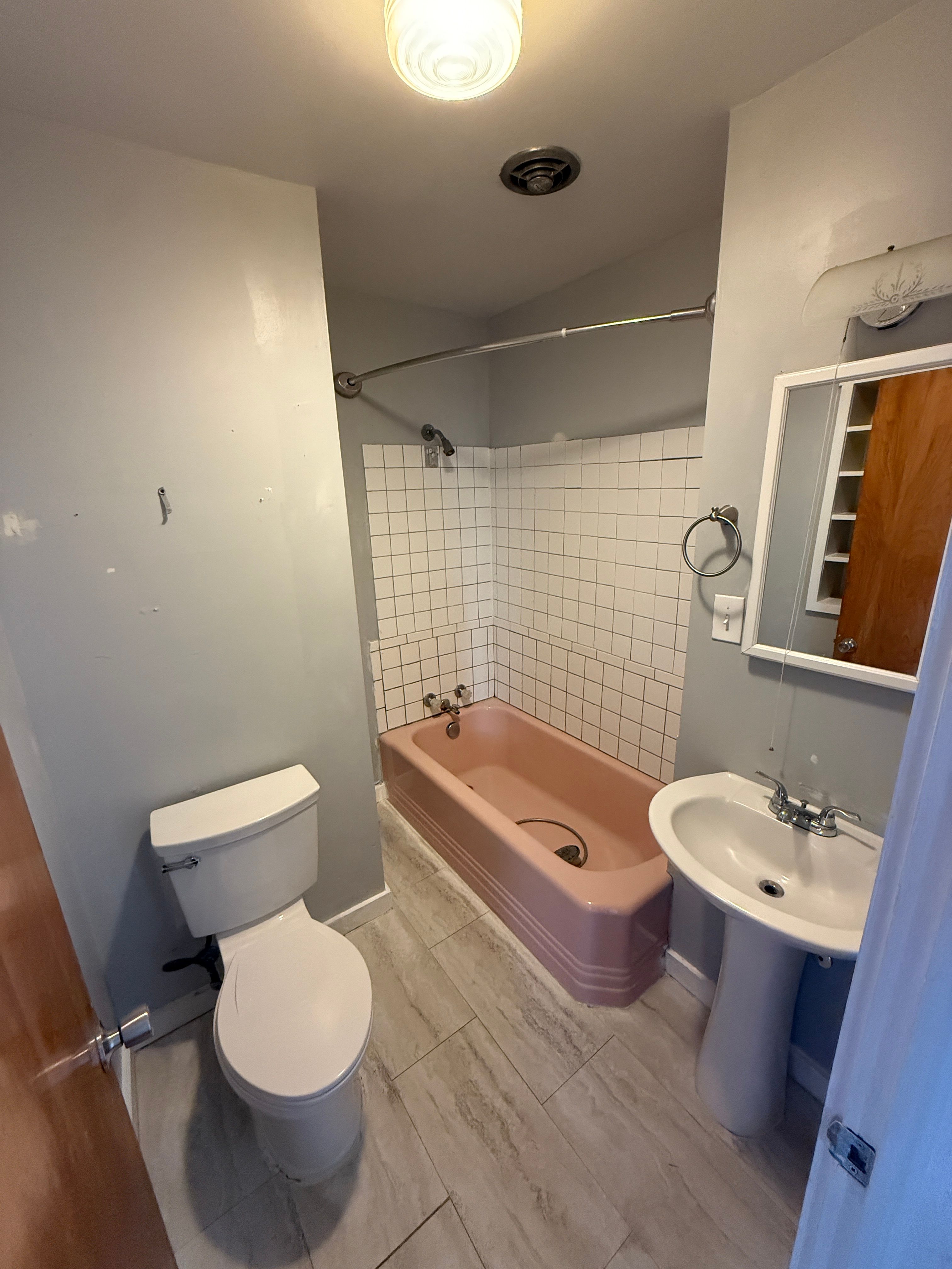 Bathroom featuring a pedestal sink, a toilet, a pink bathtub with white subway tile surround, and wood-finish flooring