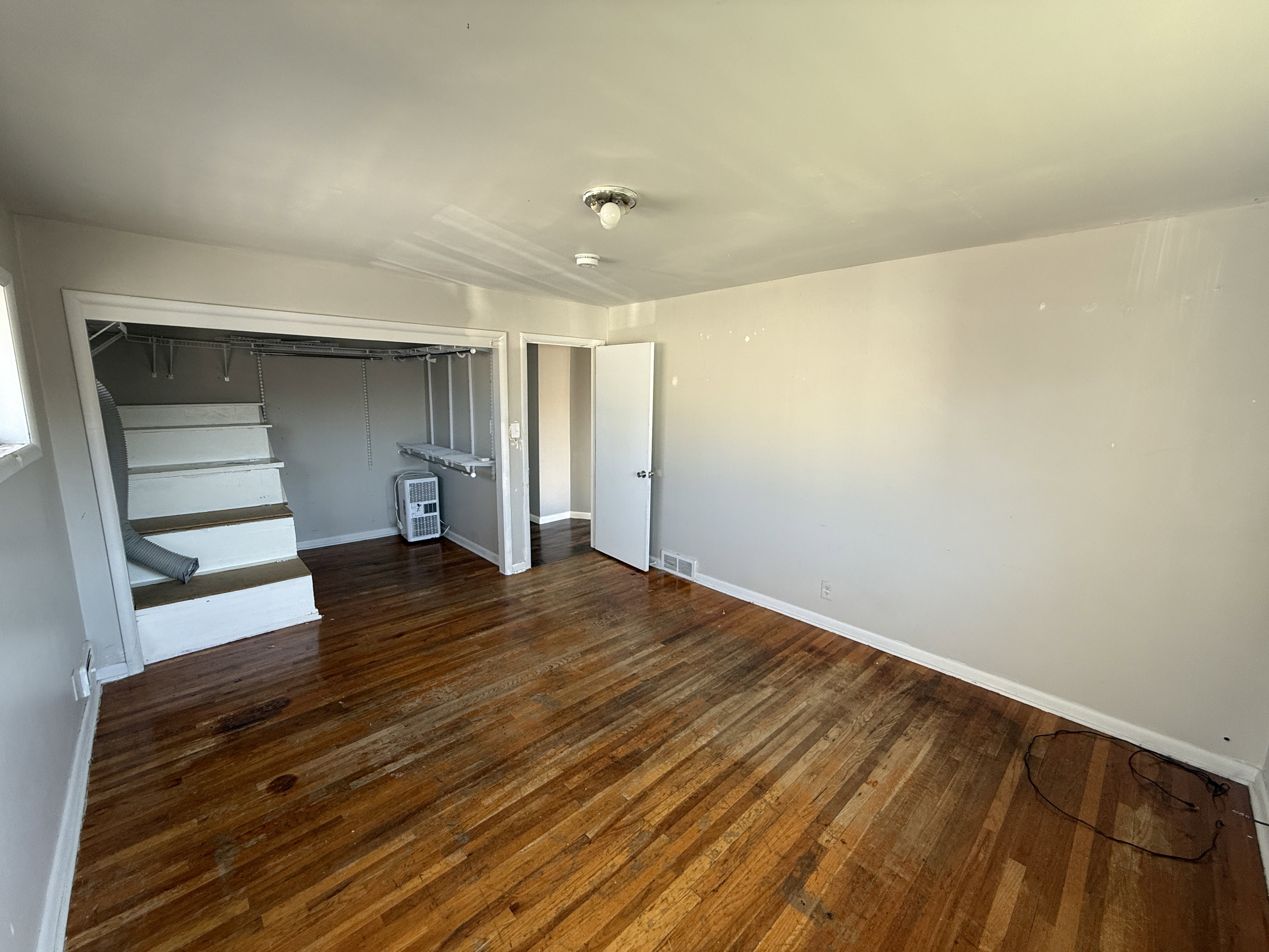 Wood-finish flooring throughout, featuring a staircase with white risers and a white door leading to another area