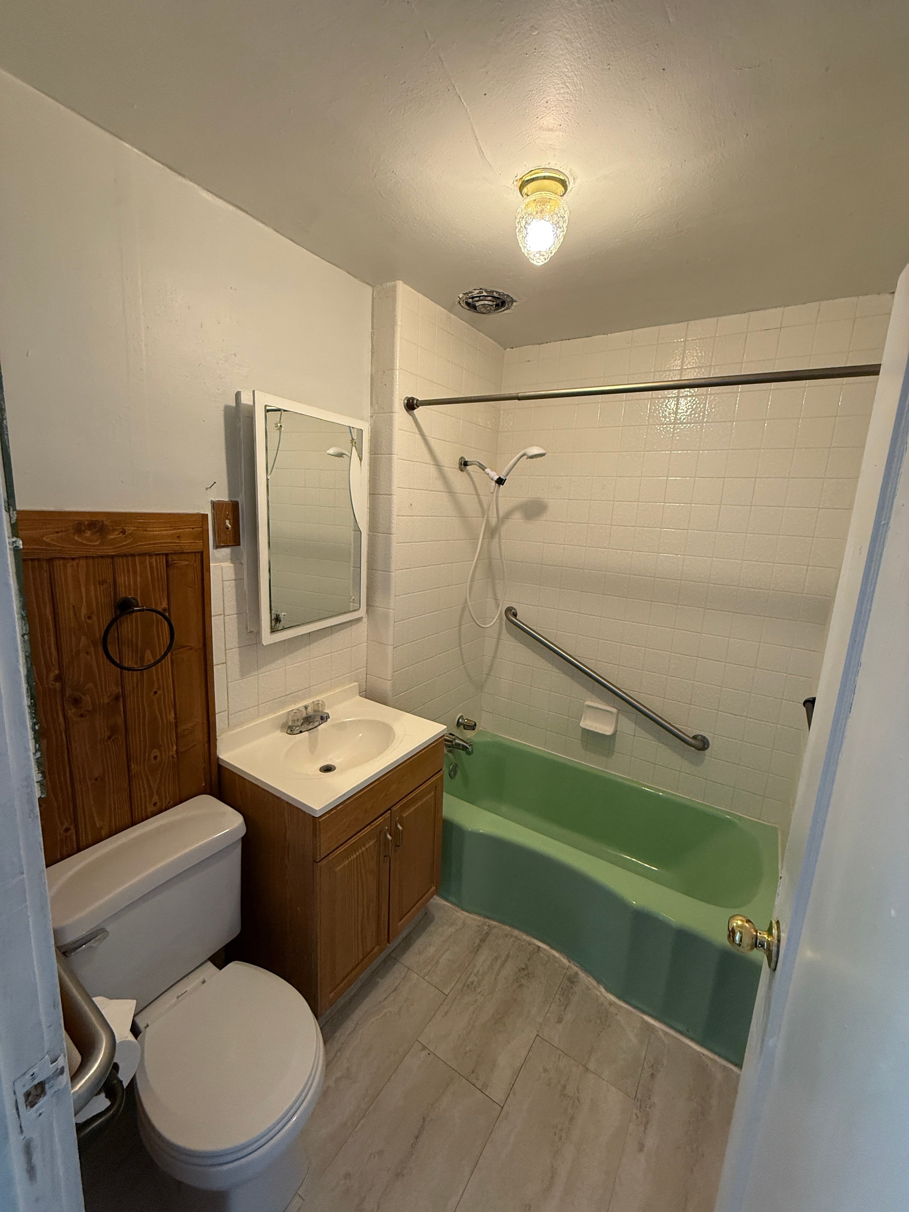 Bathroom with a green bathtub, white subway tile surround, and a chrome grab bar