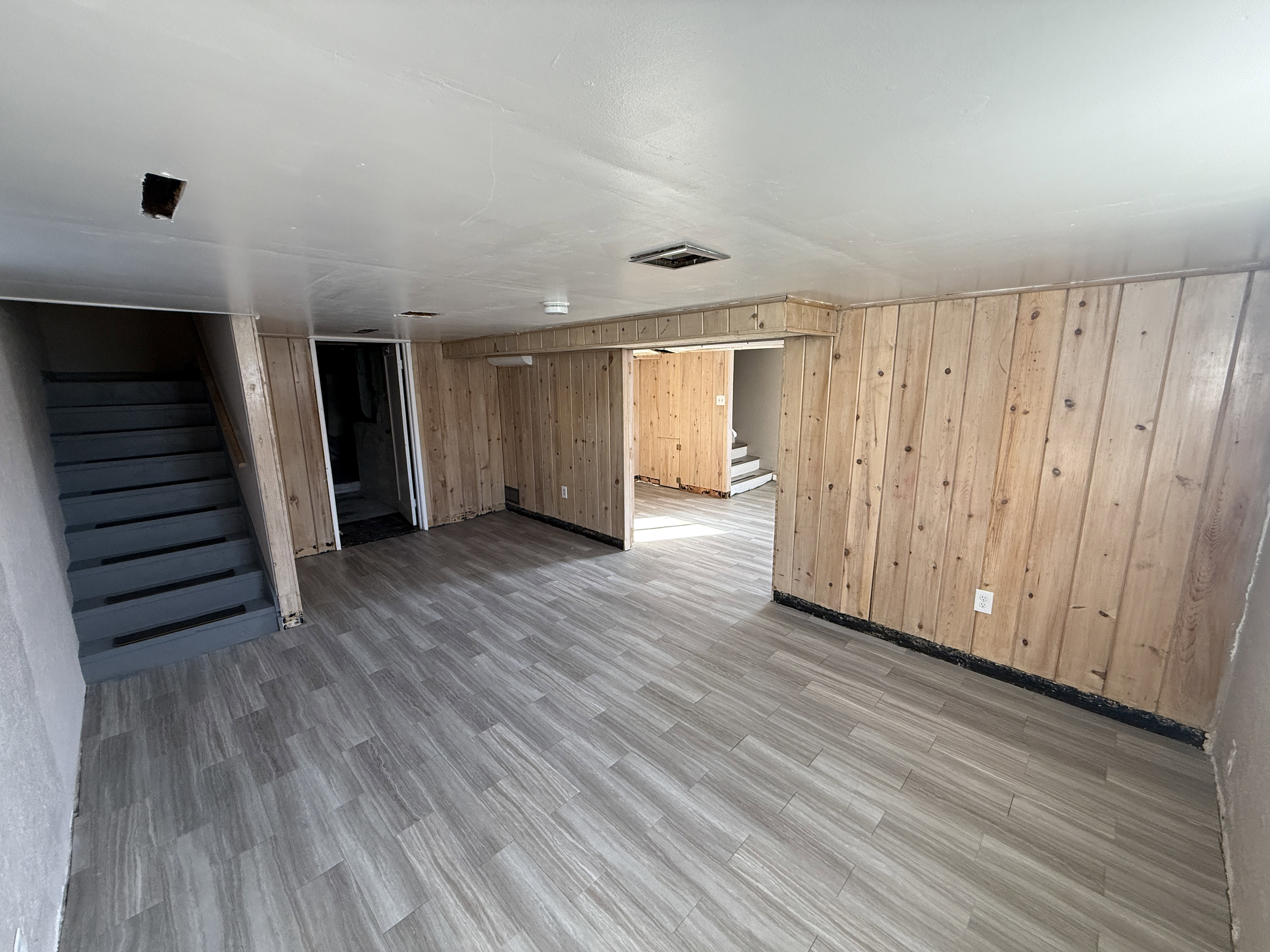 Open finished basement space featuring wood-finish paneling, light-toned plank flooring, and painted stairs