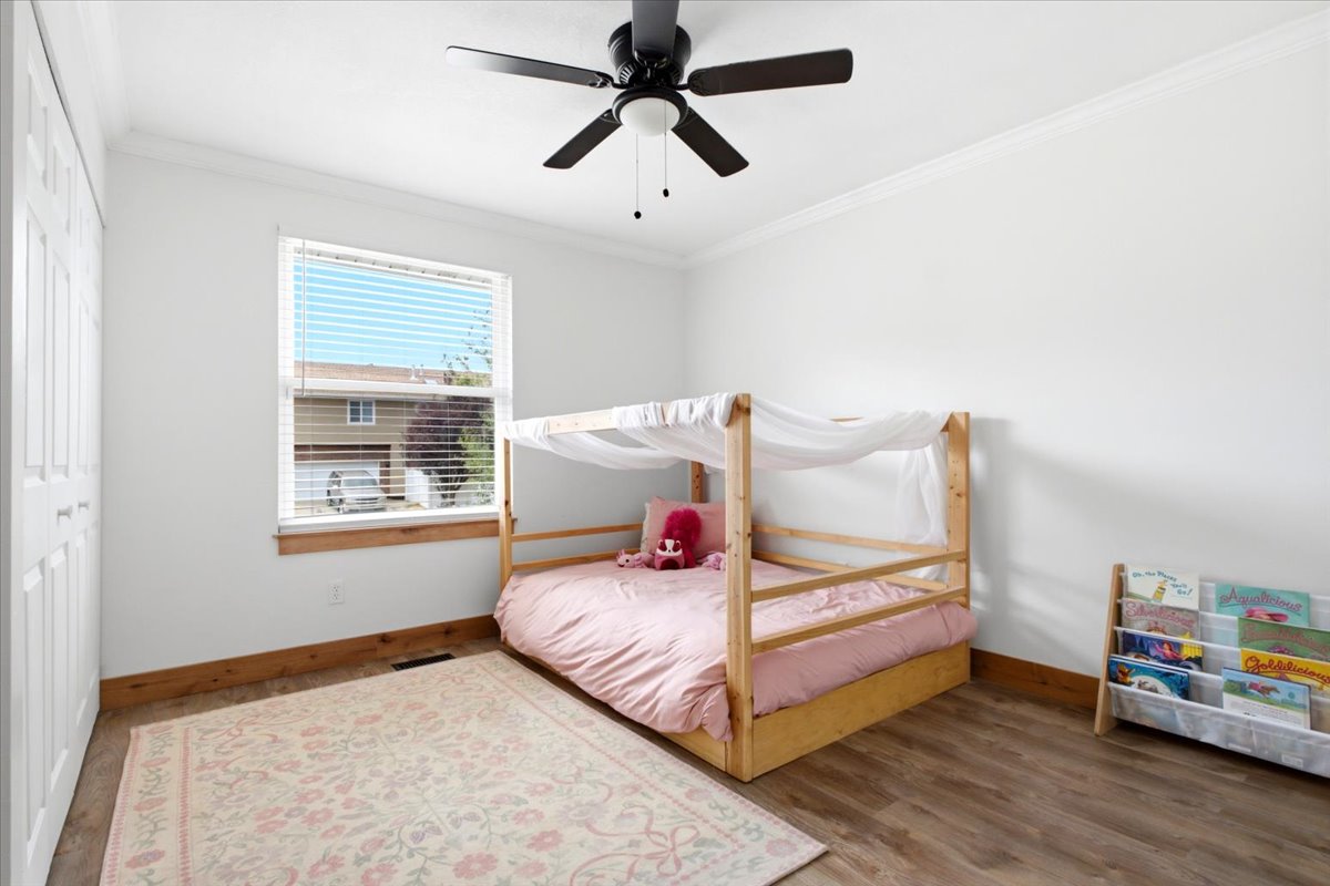 Bright room featuring a ceiling fan, wood-finish flooring, white walls, crown molding, and a window with horizontal blinds