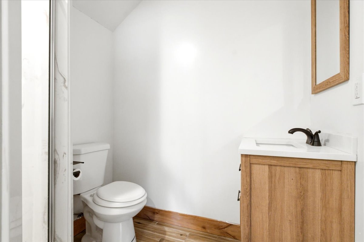 3/4 Bath-Lower level featuring a wood-finish vanity with a white countertop, bronze-finish faucet, and a wall-mounted mirror
