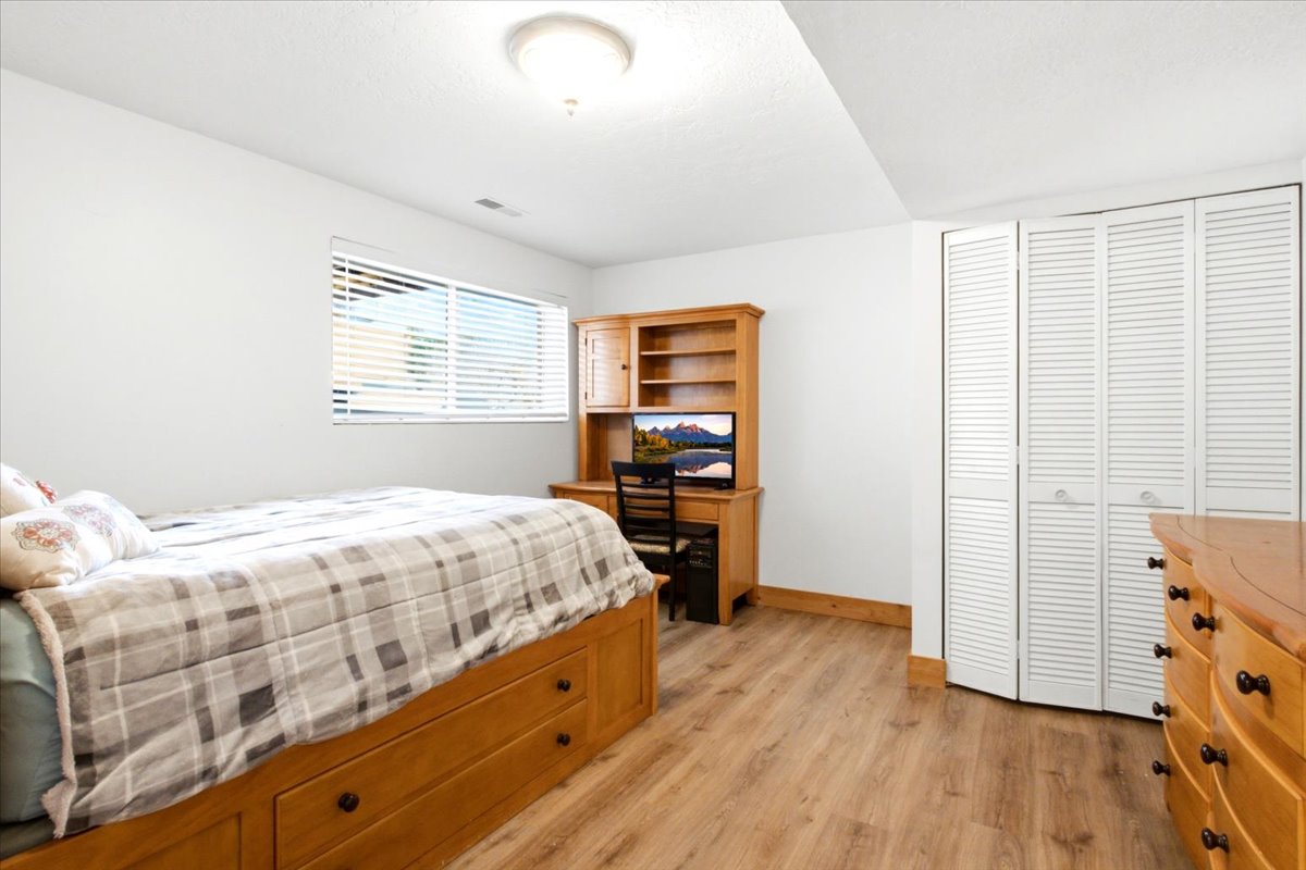 Bedroom 4 - Lower level featuring wood-finish flooring, white louvered bi-fold closet doors, and a window with horizontal blinds