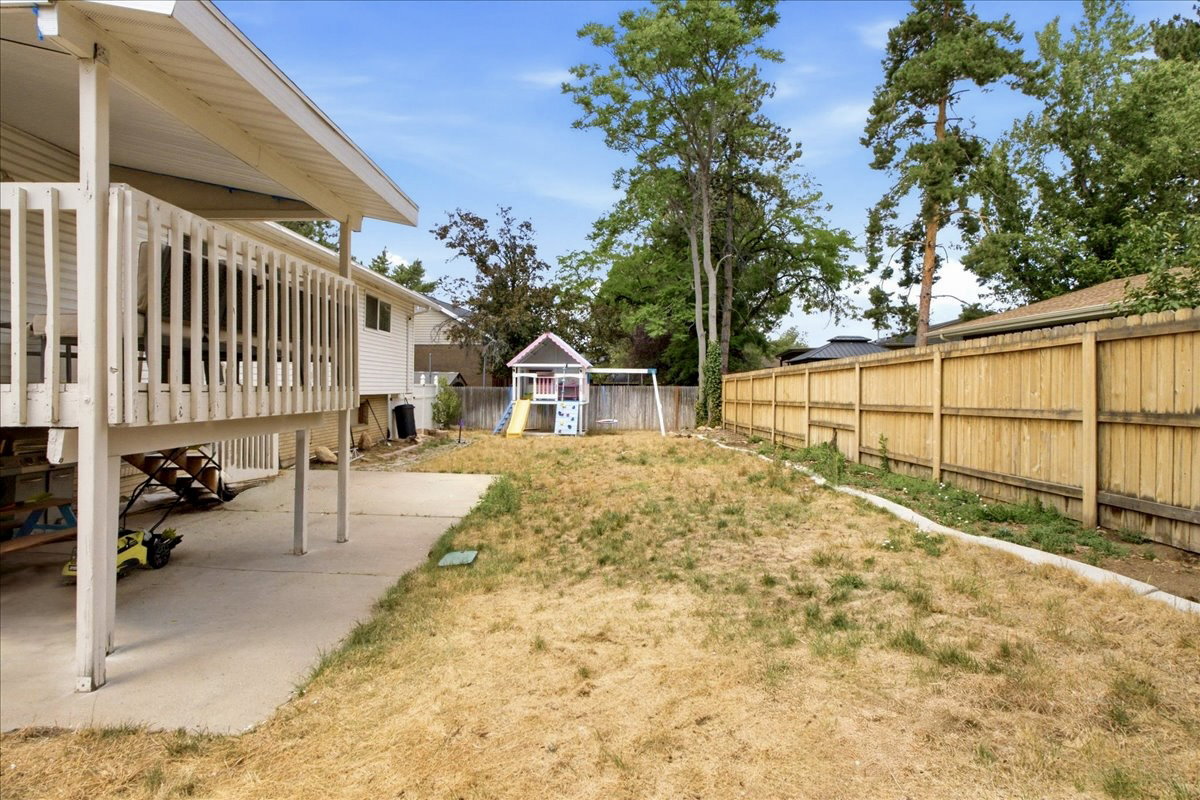 Expansive backyard featuring a concrete patio, elevated deck with white railing, and a tall wood privacy fence