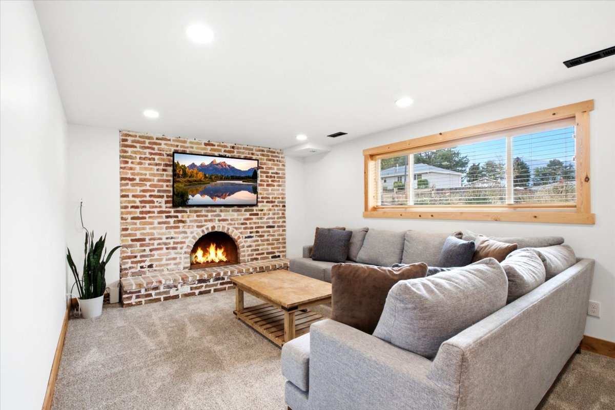 Living space featuring a brick fireplace with an arched firebox, mounted television, and a wood-framed window