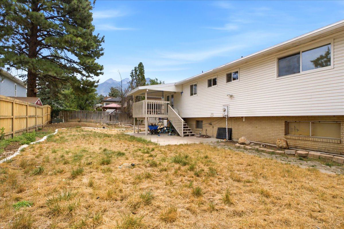 Expansive backyard space with a wood privacy fence, featuring a covered deck with stairs, a patio area, and a large mature tree