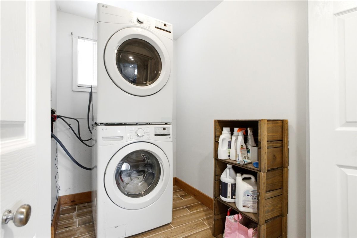 Dedicated laundry area featuring a stacked washer and dryer unit, wood-finish tile flooring, white walls, and a window providing natural light