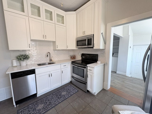 Contemporary kitchen featuring white cabinetry, subway tile backsplash, stainless steel appliances including a microwave, oven/range, and dishwasher, and light-toned countertops