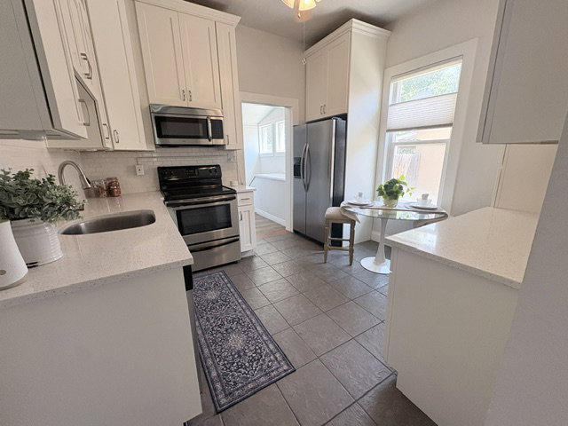 Kitchen featuring white shaker cabinetry, stainless steel appliances, a tile backsplash, light-toned countertops, and tile flooring