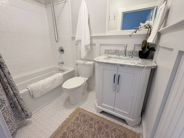 White subway tile shower surround with a built-in tub, white vanity with a stone countertop, chrome fixtures, and hexagon tile flooring