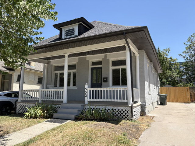 Gray painted brick exterior featuring a covered front porch with white columns, a dark gray roof, and a visible dormer