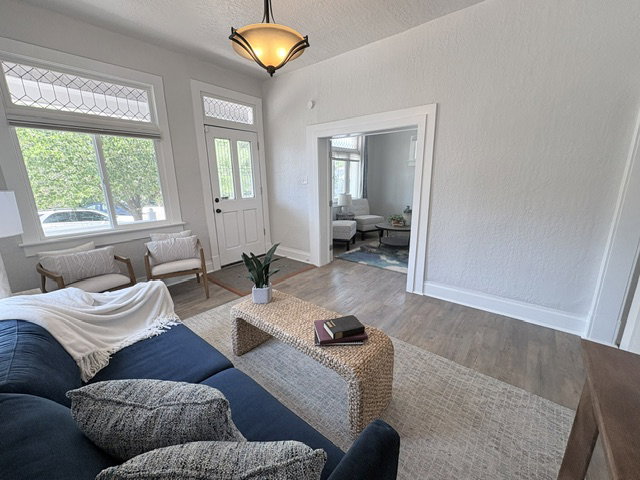 Spacious living area featuring wood-finish flooring, white trim, and a prominent front entry door with transom window