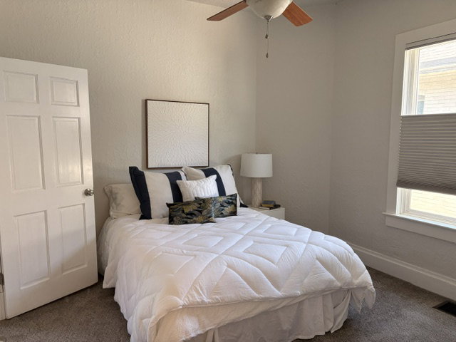 Neutral-toned room featuring a panel door, a window with cellular shades, a ceiling fan, and carpeted flooring