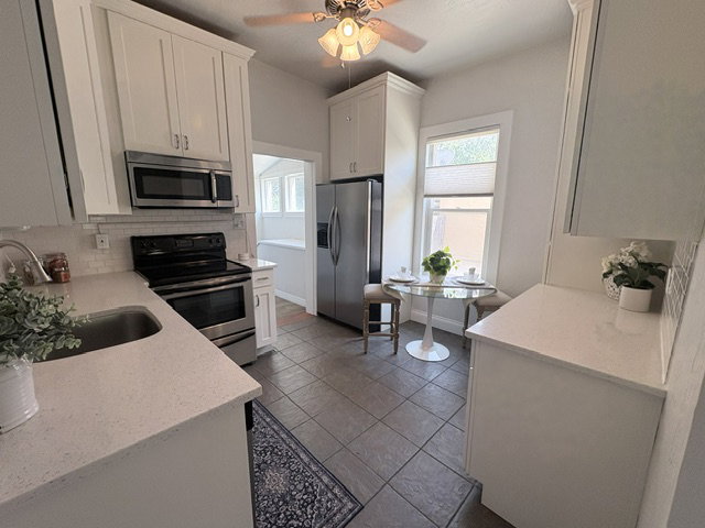 Kitchen featuring white cabinetry, stainless steel appliances, light-toned countertops, and a subway tile backsplash