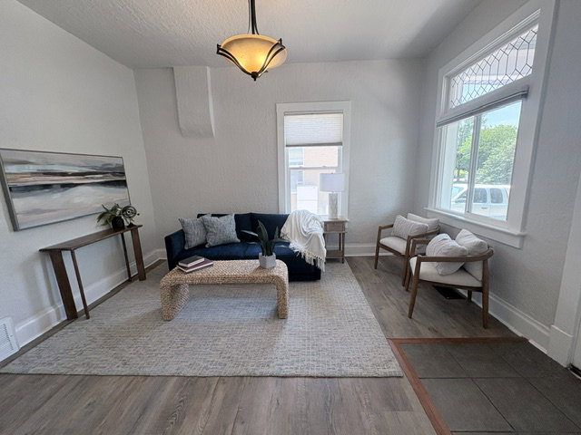 Bright living area featuring wood-finish flooring, a decorative transom window, an overhead light fixture, white baseboards, and textured walls