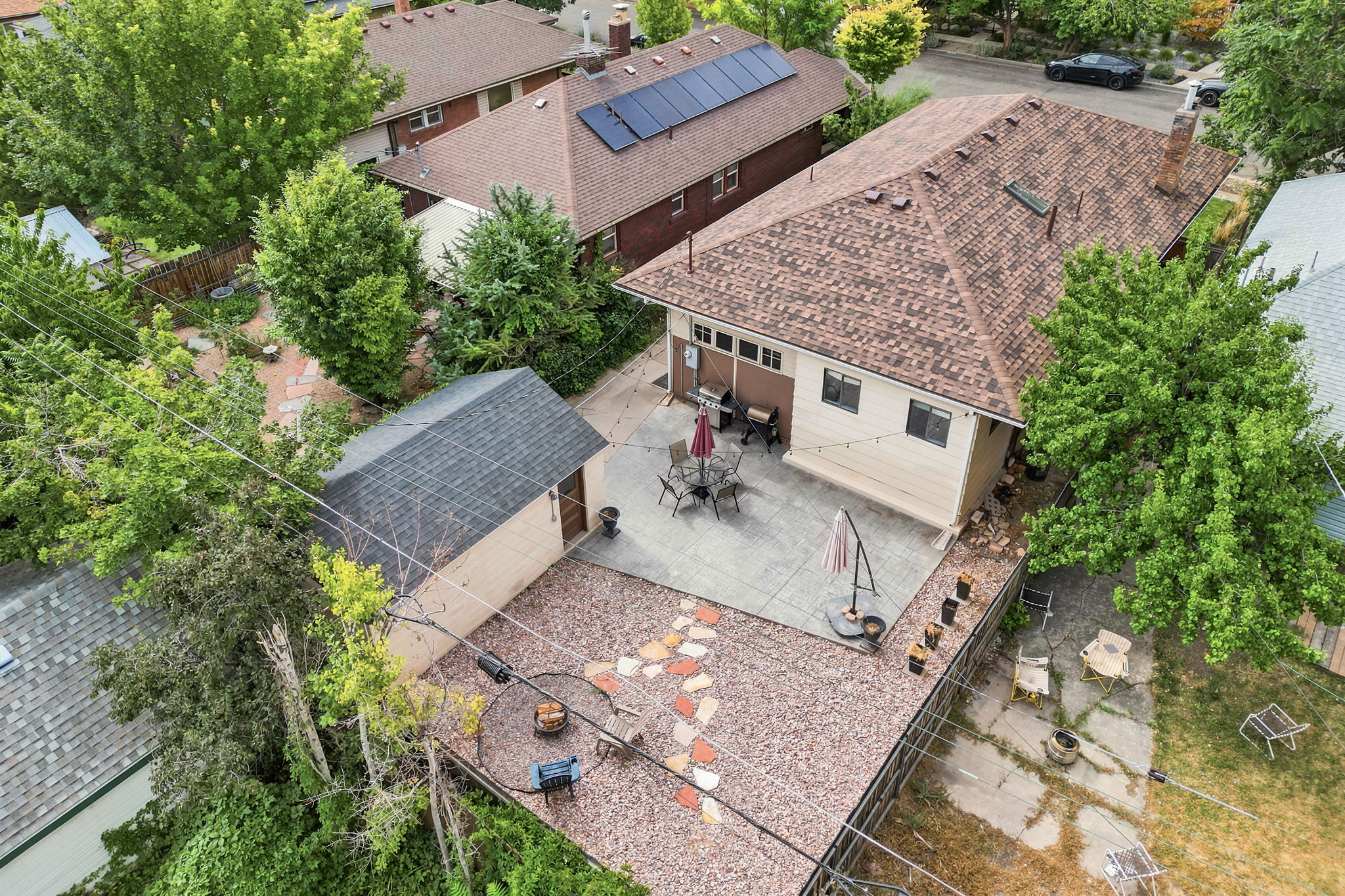 Expansive rear yard featuring a concrete patio with perimeter string lighting, a gravel area with stepping stones, and a detached shed with an asphalt shingle roof