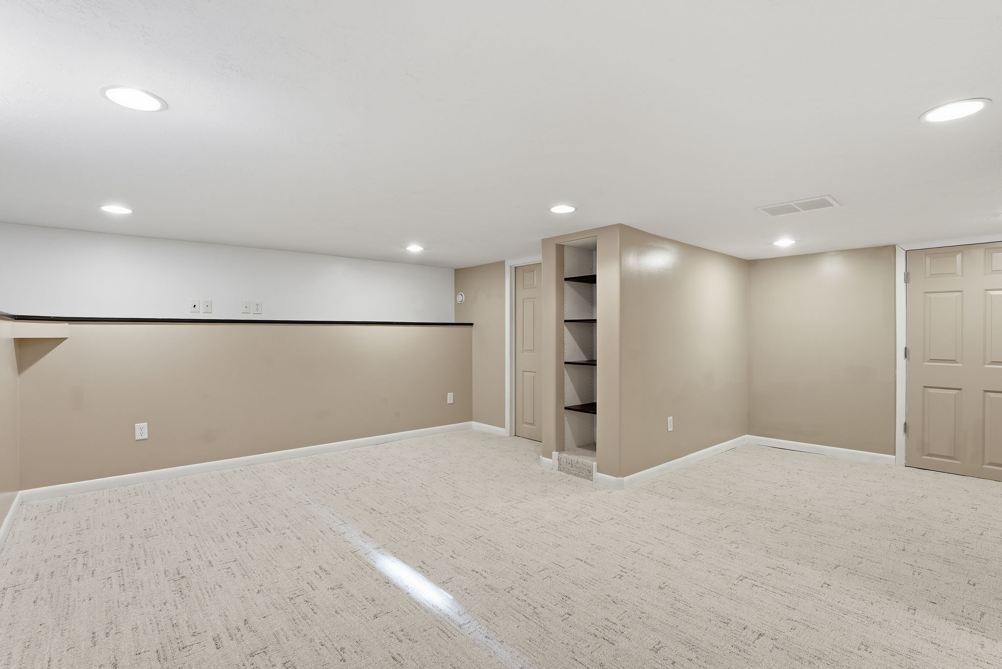 Spacious room featuring neutral carpeting, recessed lighting, built-in shelving, and two paneled doors