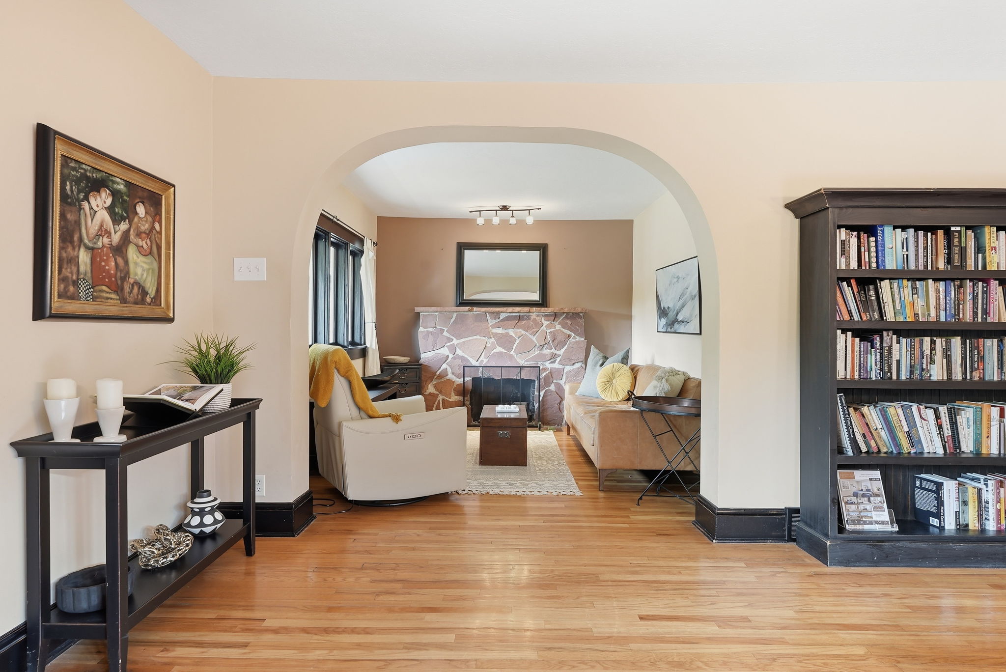 Hardwood flooring extends from the foreground into an arched doorway, revealing a living area with a stone-clad fireplace and dark trim
