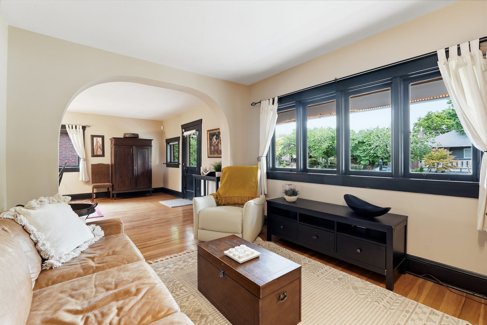 Bright living area featuring wood-finish flooring, a large multi-pane window, an arched doorway, and light-toned wall paint