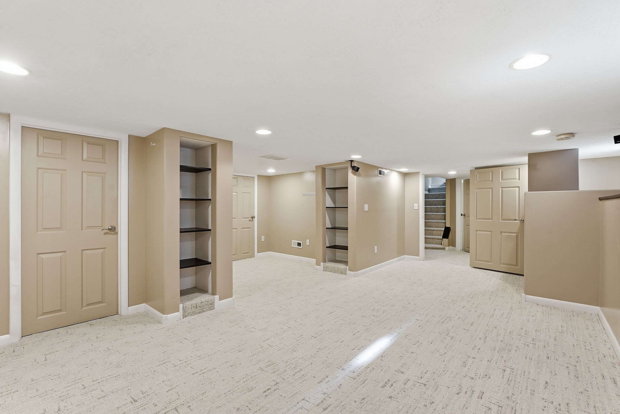 Spacious carpeted room featuring recessed lighting, built-in shelving, paneled doors, and painted walls
