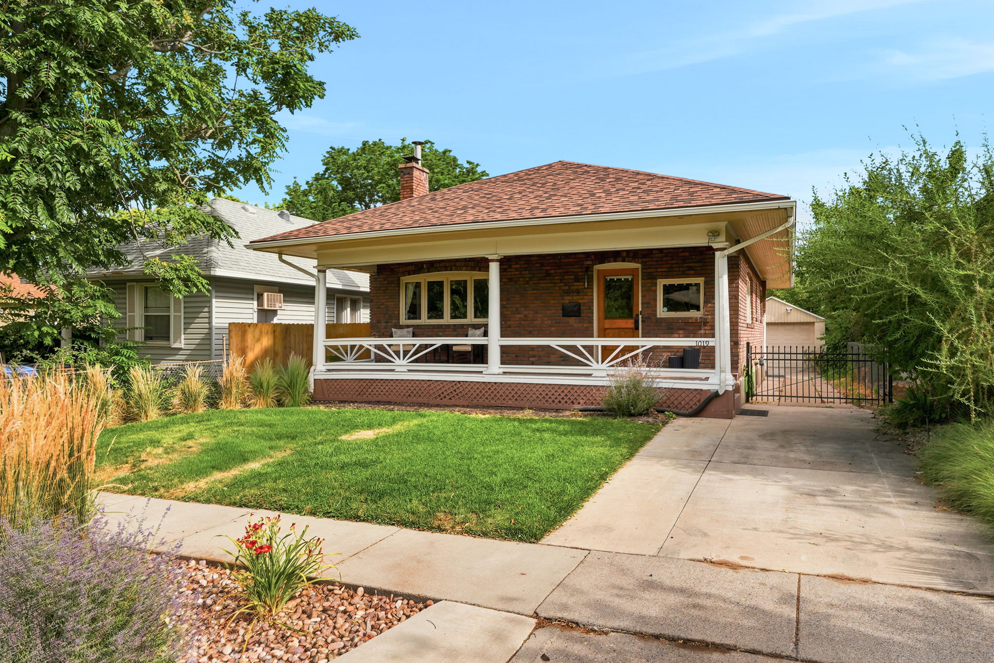 Brick facade residence featuring a covered front porch with decorative railing, shingle roof, and a paved driveway leading to a rear garage