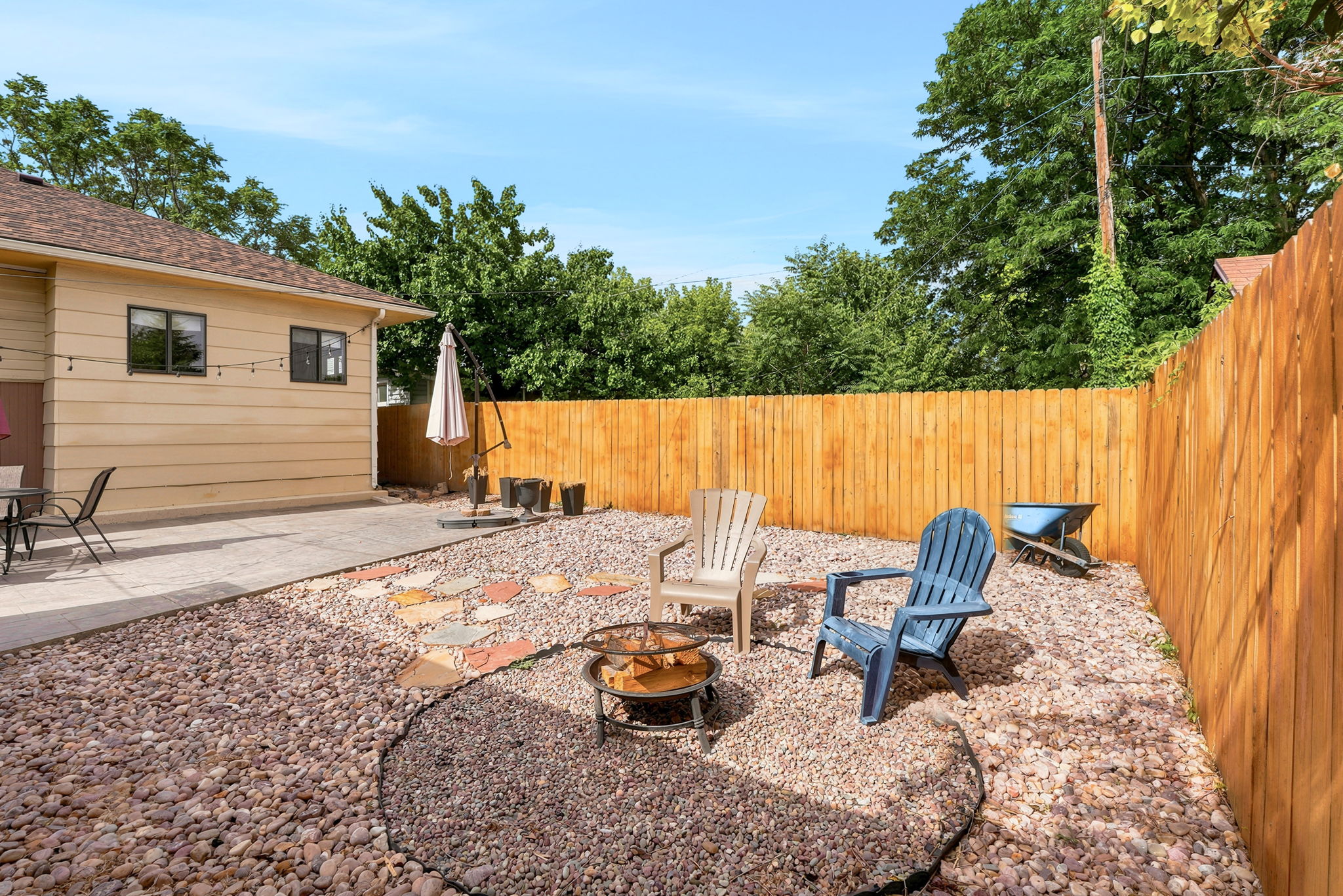 Spacious backyard featuring a large concrete patio, a gravel hardscaping area, a fire pit, and a tall wood privacy fence