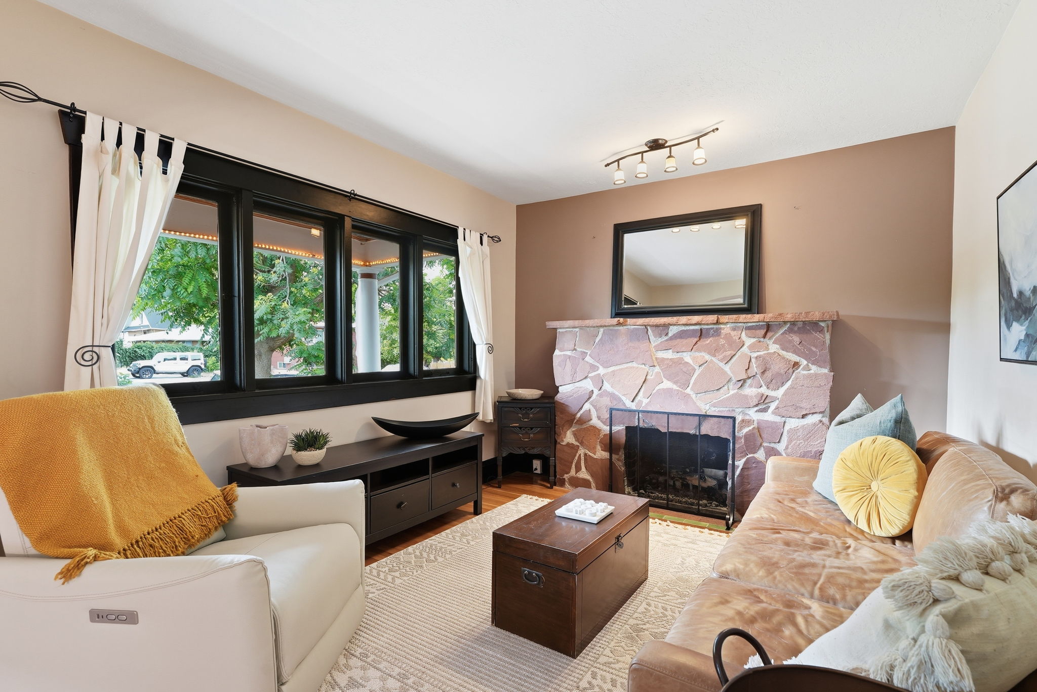 Living area featuring a natural stone fireplace, wood-finish flooring, and multiple dark-framed windows