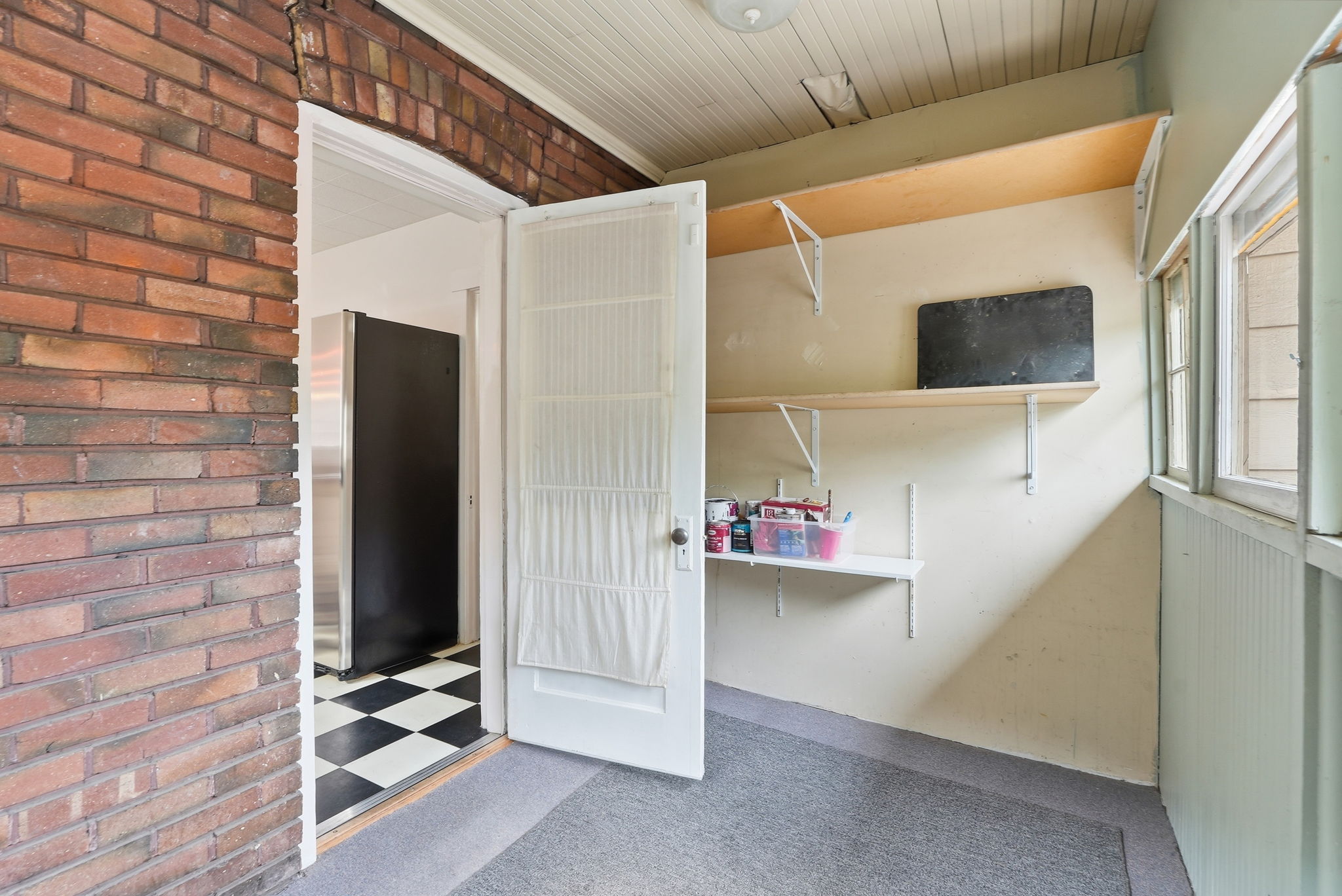Enclosed entryway featuring brick wall accents, wood-paneled ceiling, and a doorway opening to an interior space with checkerboard flooring