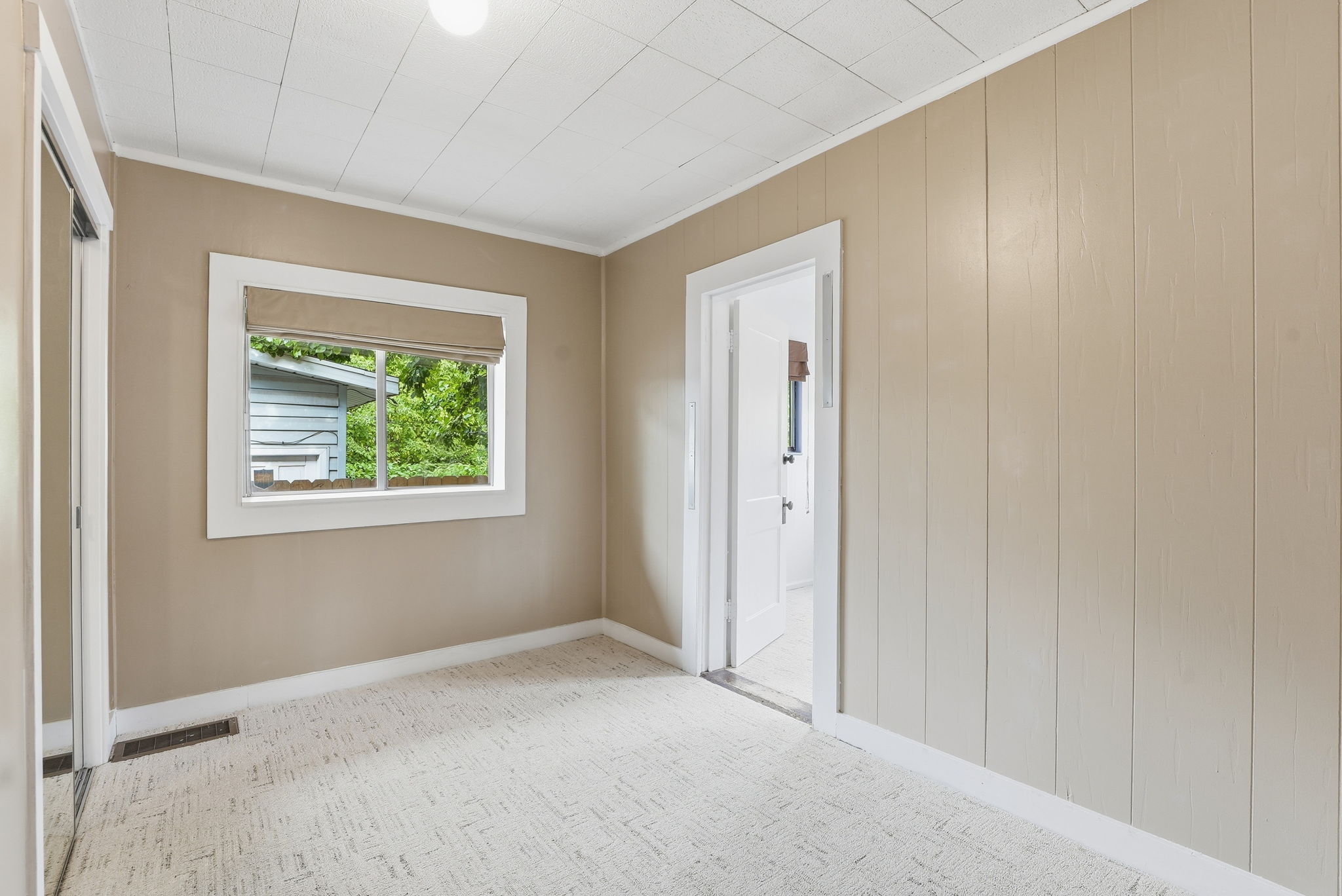 Light-filled room featuring a single window, neutral wall paneling, and a panelled ceiling