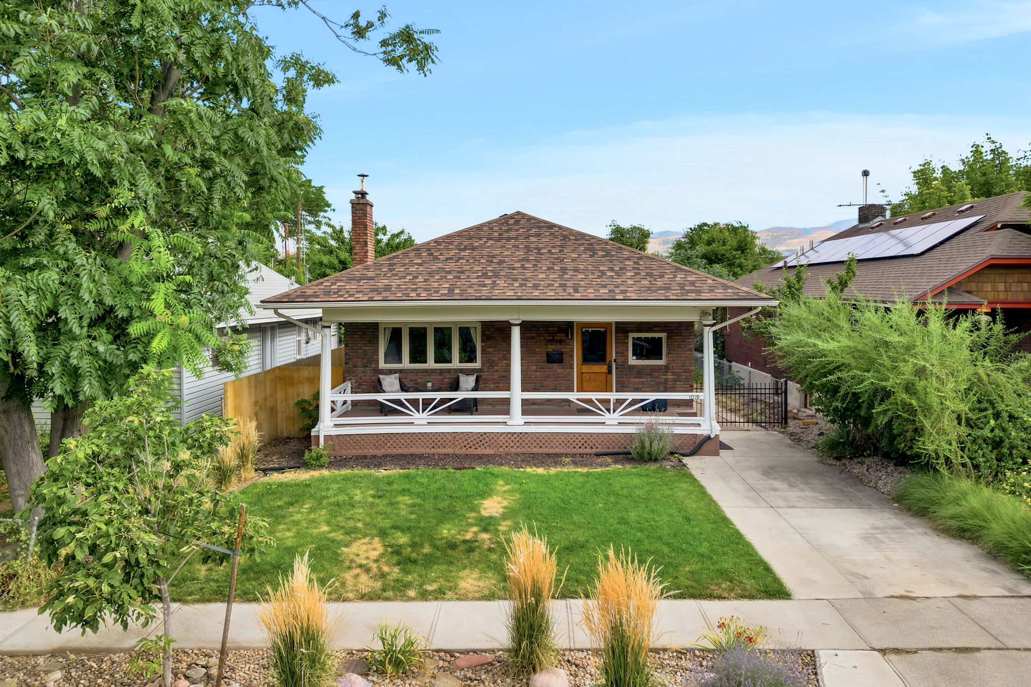 Brick facade home featuring a covered front porch with white railing, a dormer roof, and a mature front yard