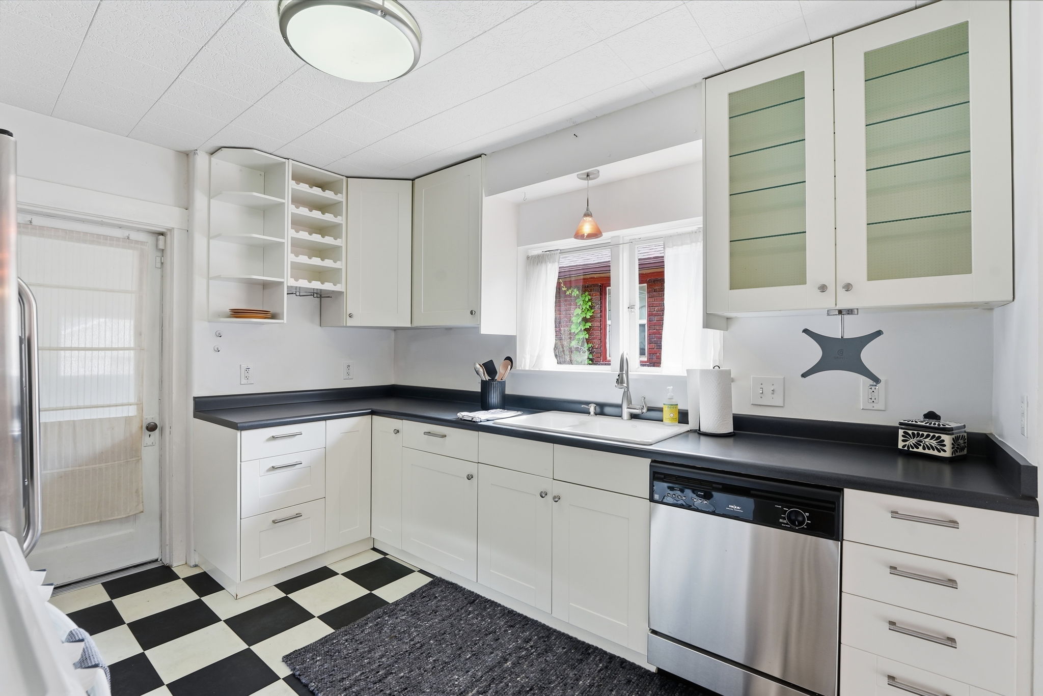 Kitchen featuring white cabinetry, black countertops, a built-in stainless steel dishwasher, a window over the sink, and checkerboard floor tiles