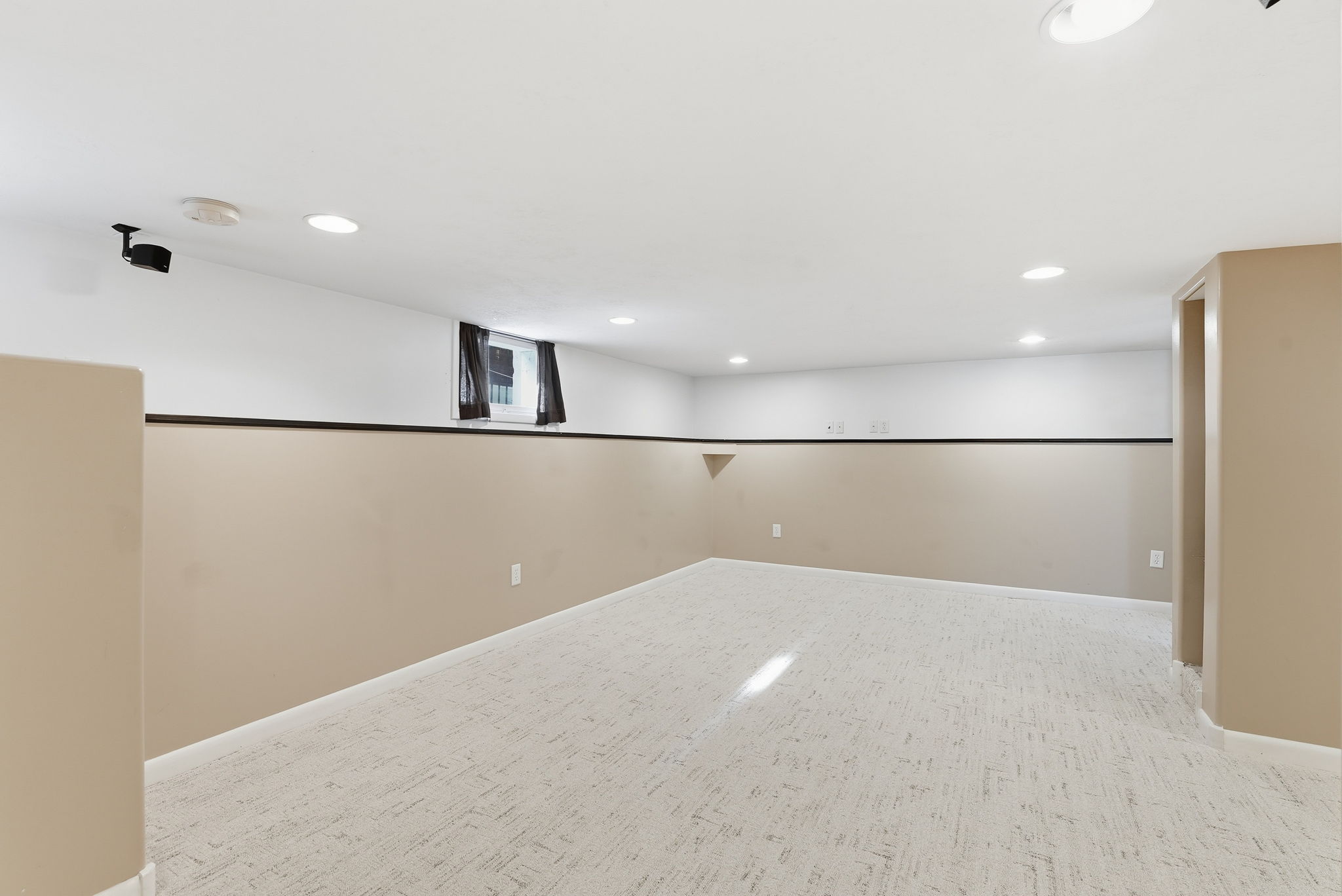 Spacious room featuring light-toned flooring, recessed lighting, a window with dark coverings, and a two-tone wall treatment with a dark trim