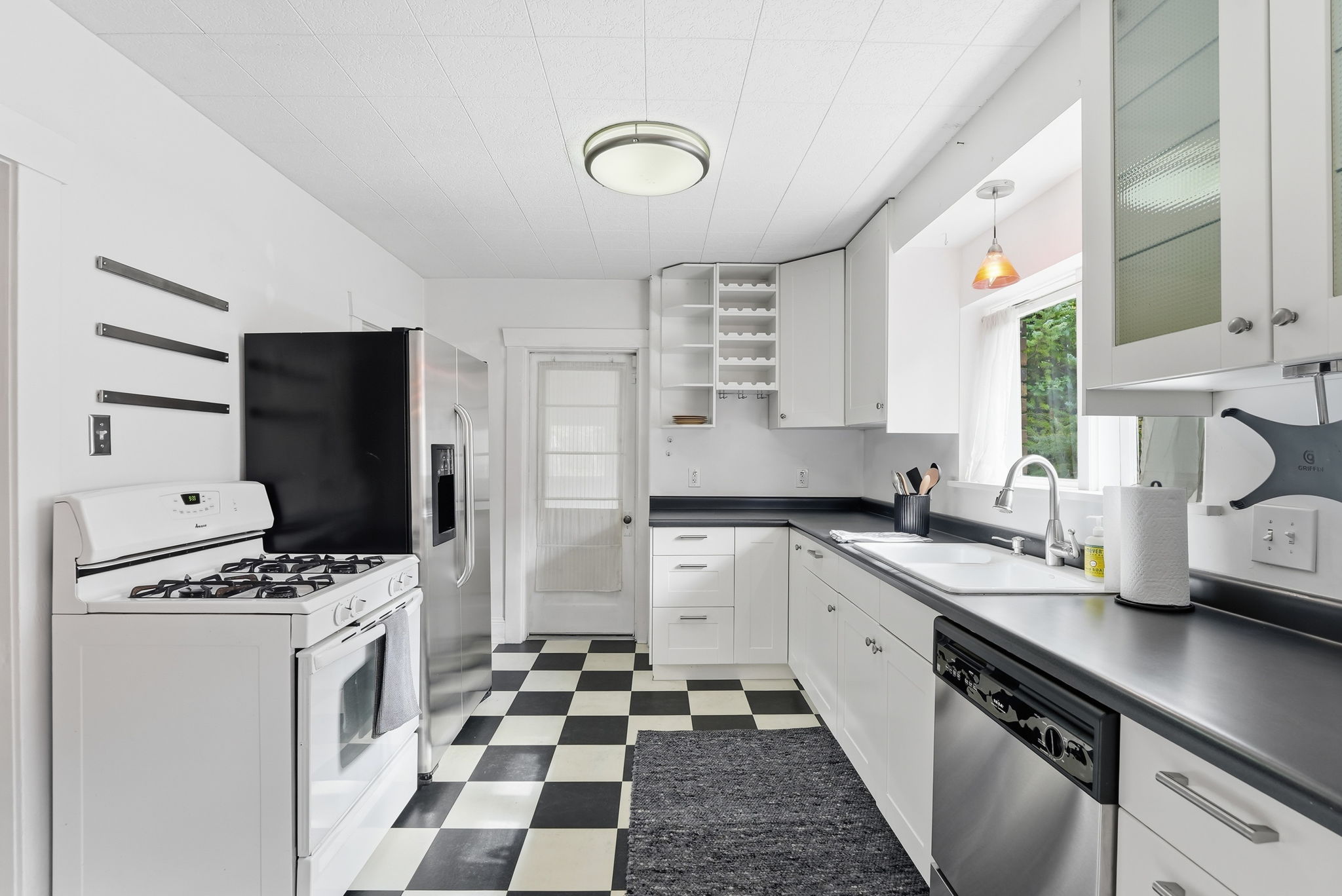 Kitchen featuring checkerboard flooring, white cabinetry, dark countertops, a stainless steel refrigerator, and a built-in dishwasher