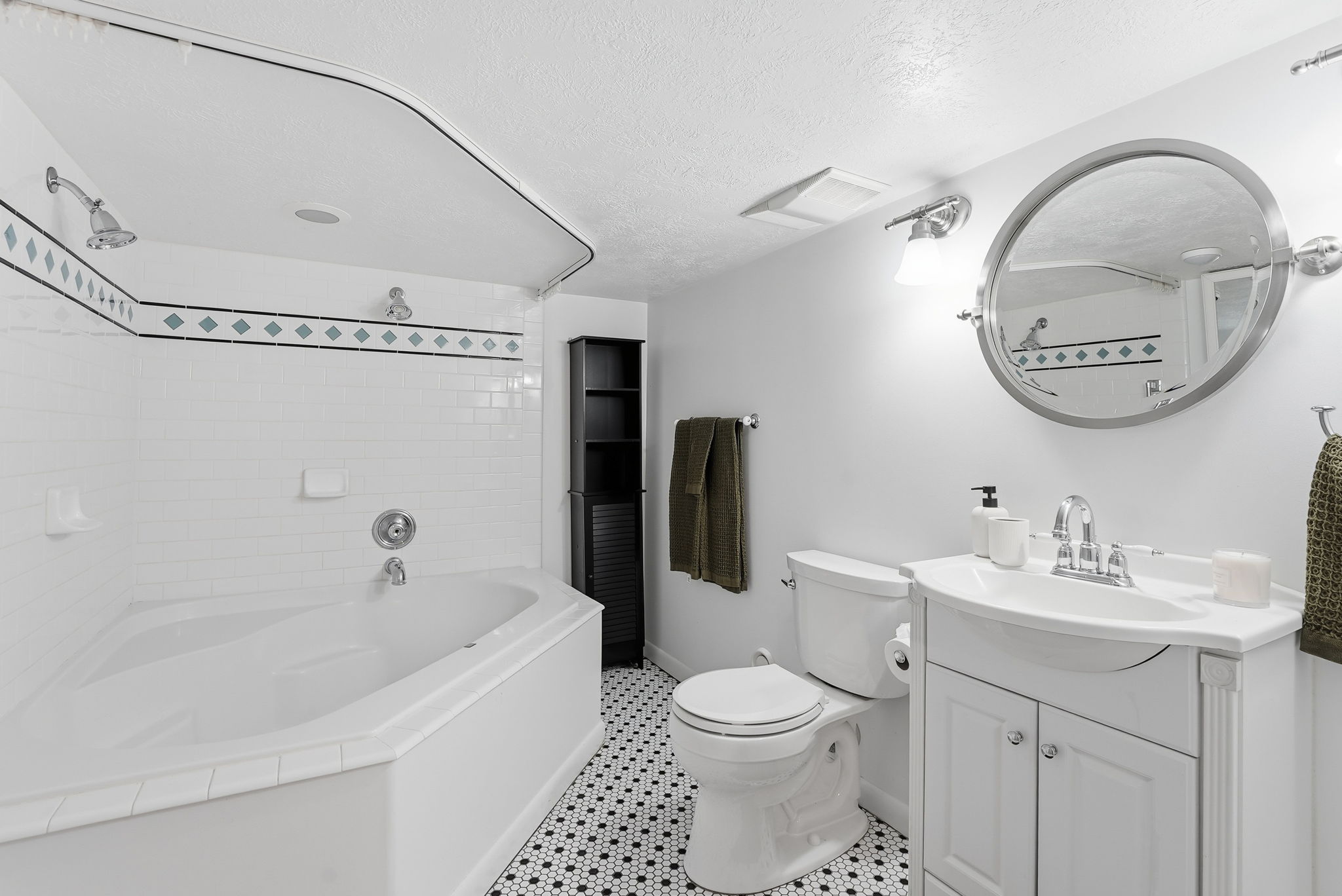Bathroom featuring a corner soaking tub with white subway tile surround, mosaic floor tiling, and a vanity with an integrated sink
