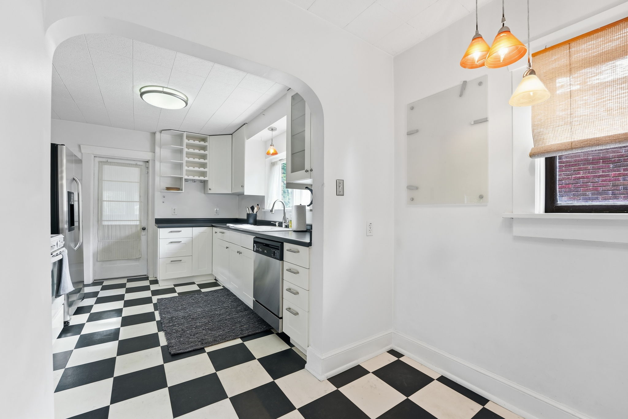 Kitchen featuring black and white checkerboard flooring, white cabinetry, dark countertops, and stainless steel appliances