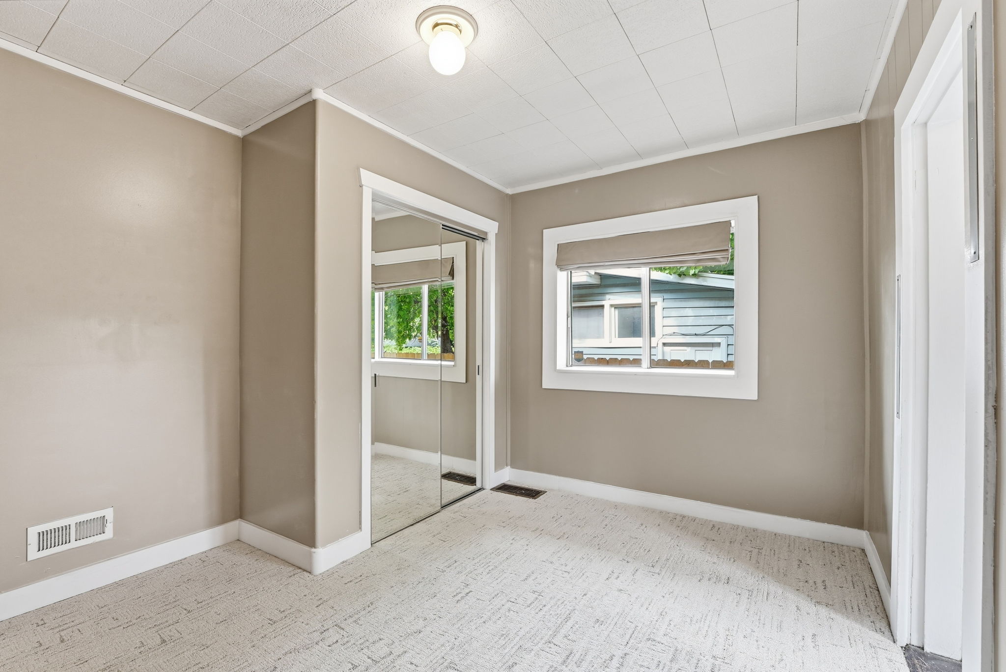 Neutral tone walls with white trim, a built-in closet featuring mirrored sliding doors, and a window with a roller shade