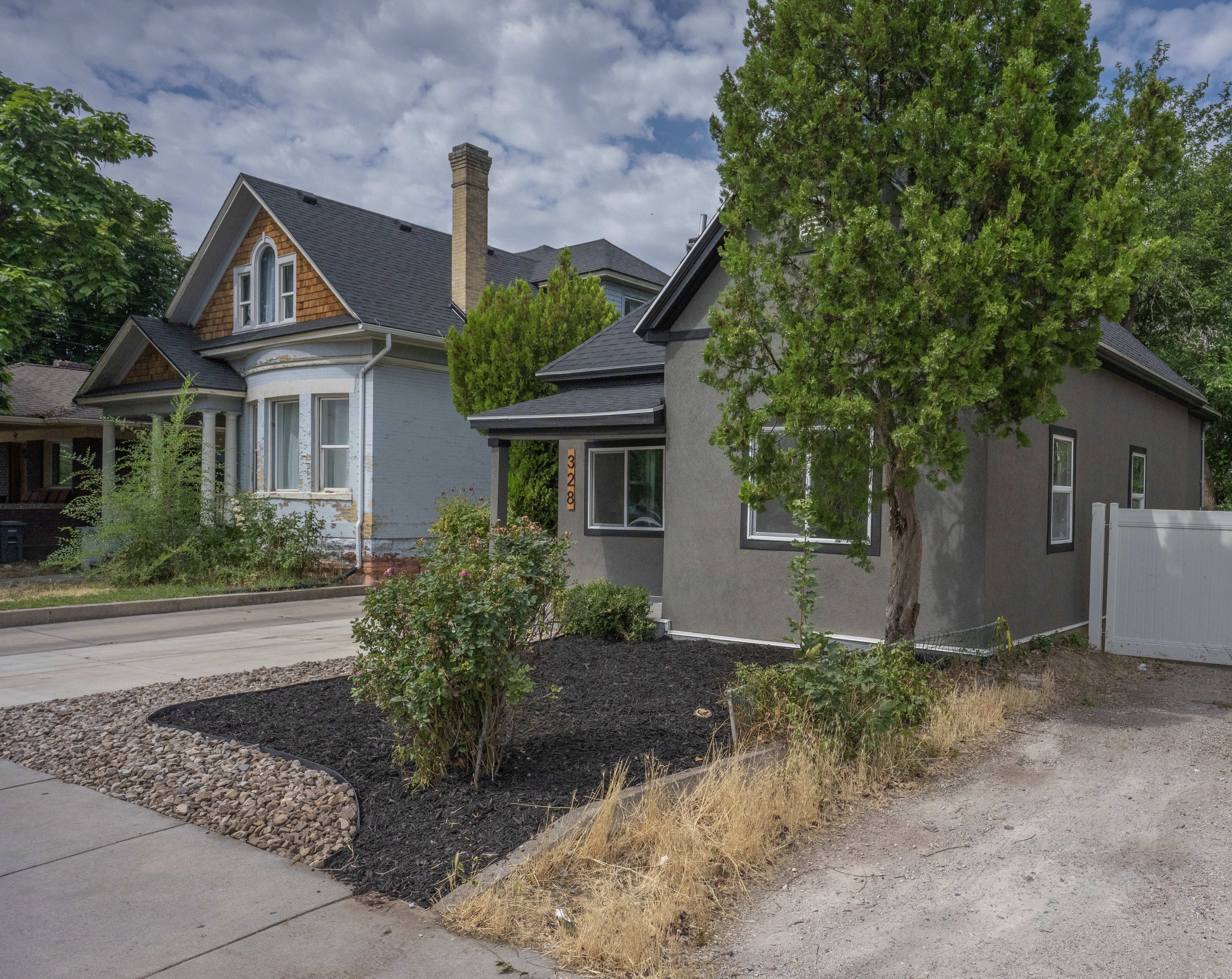 Stucco exterior with contrasting window trim, mature tree, new landscaping with dark mulch and decorative stone, and a private side fence