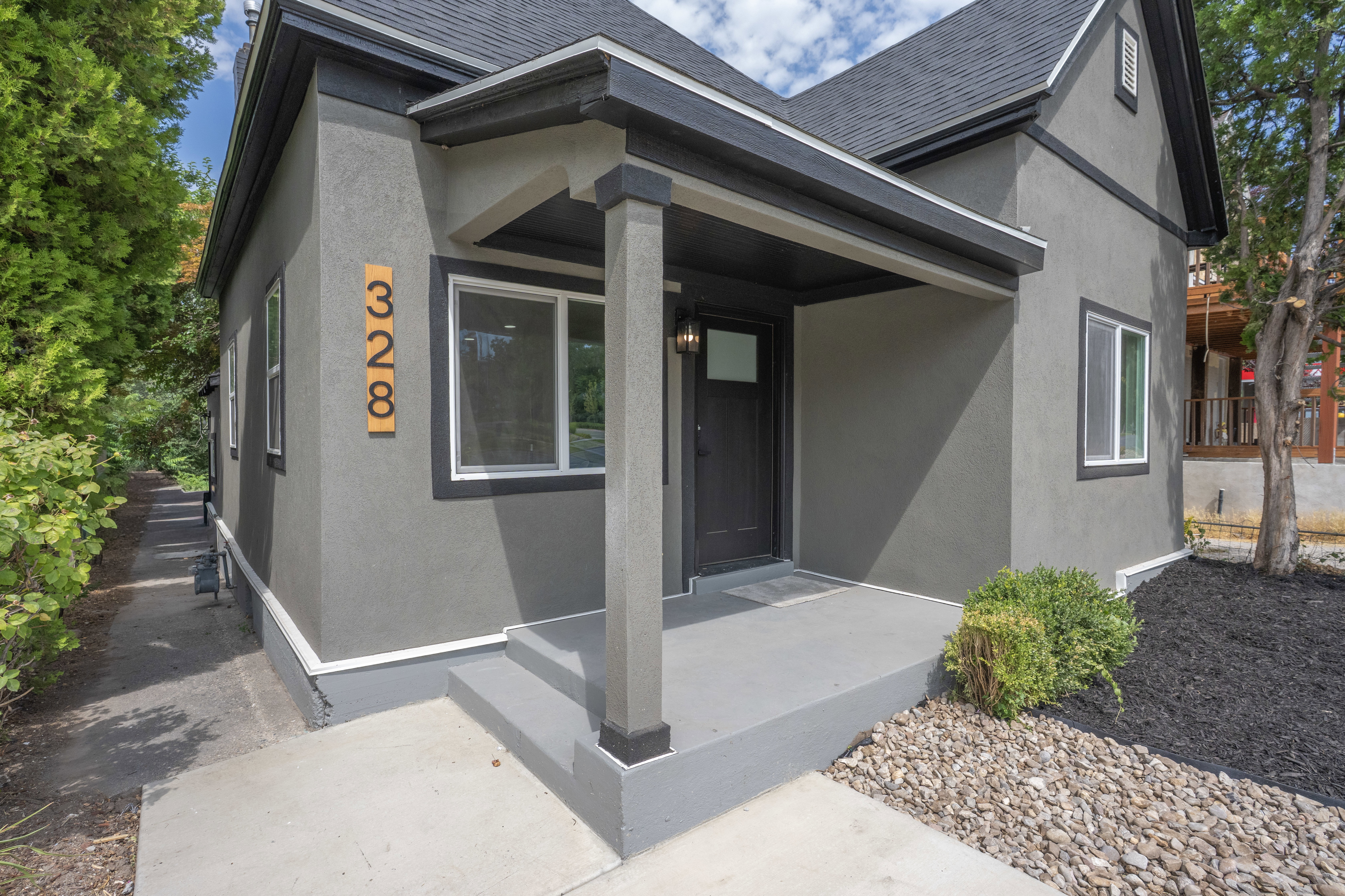 Contemporary exterior featuring a covered porch, dark gray stucco siding, and a dark asphalt shingle roof
