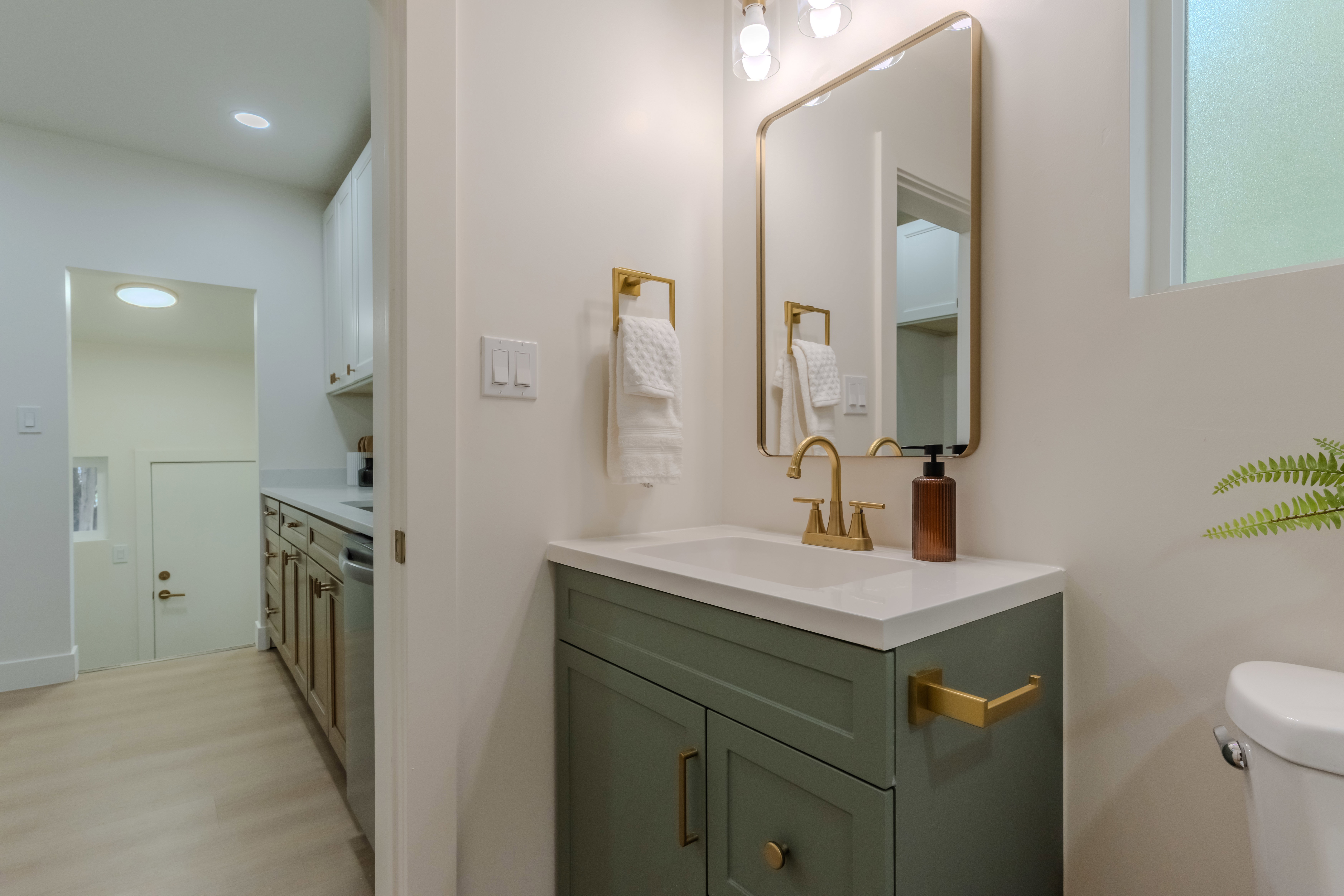 Bathroom featuring a green vanity with brass hardware, a gold-framed mirror, and a white countertop
