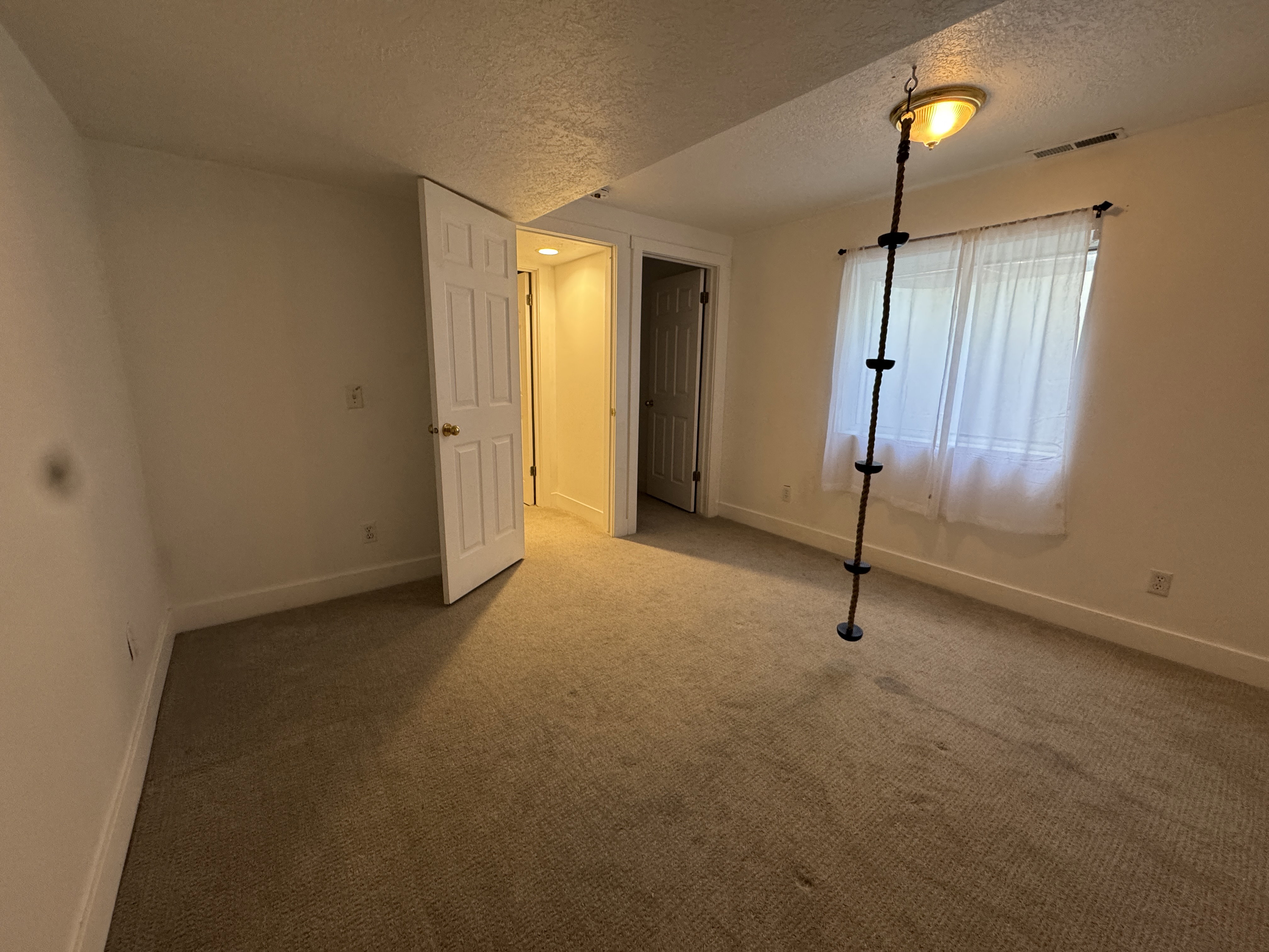 Carpeted interior space with a window featuring white sheer curtains