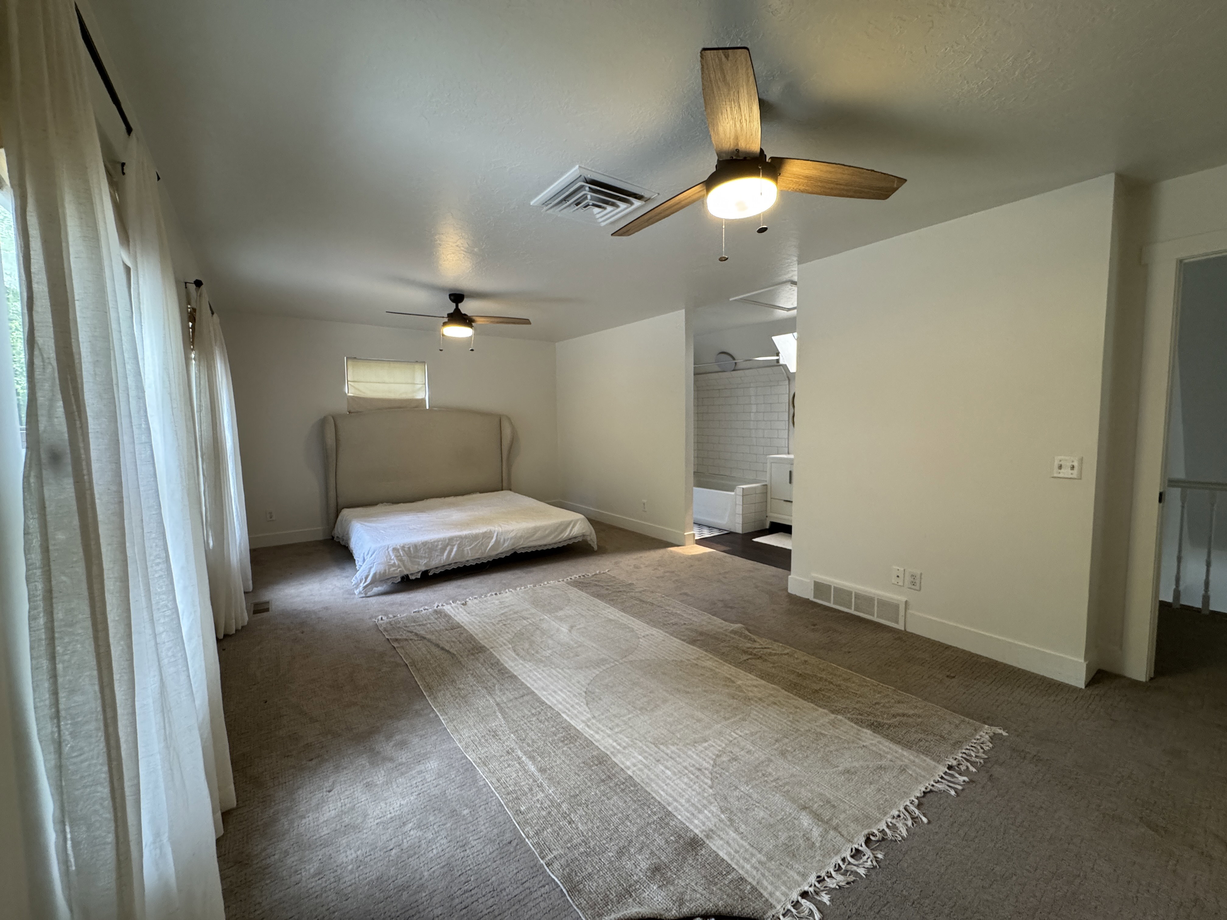 Carpeted room featuring multiple windows with sheer drapery, two ceiling fans with light fixtures, and a neutral color palette