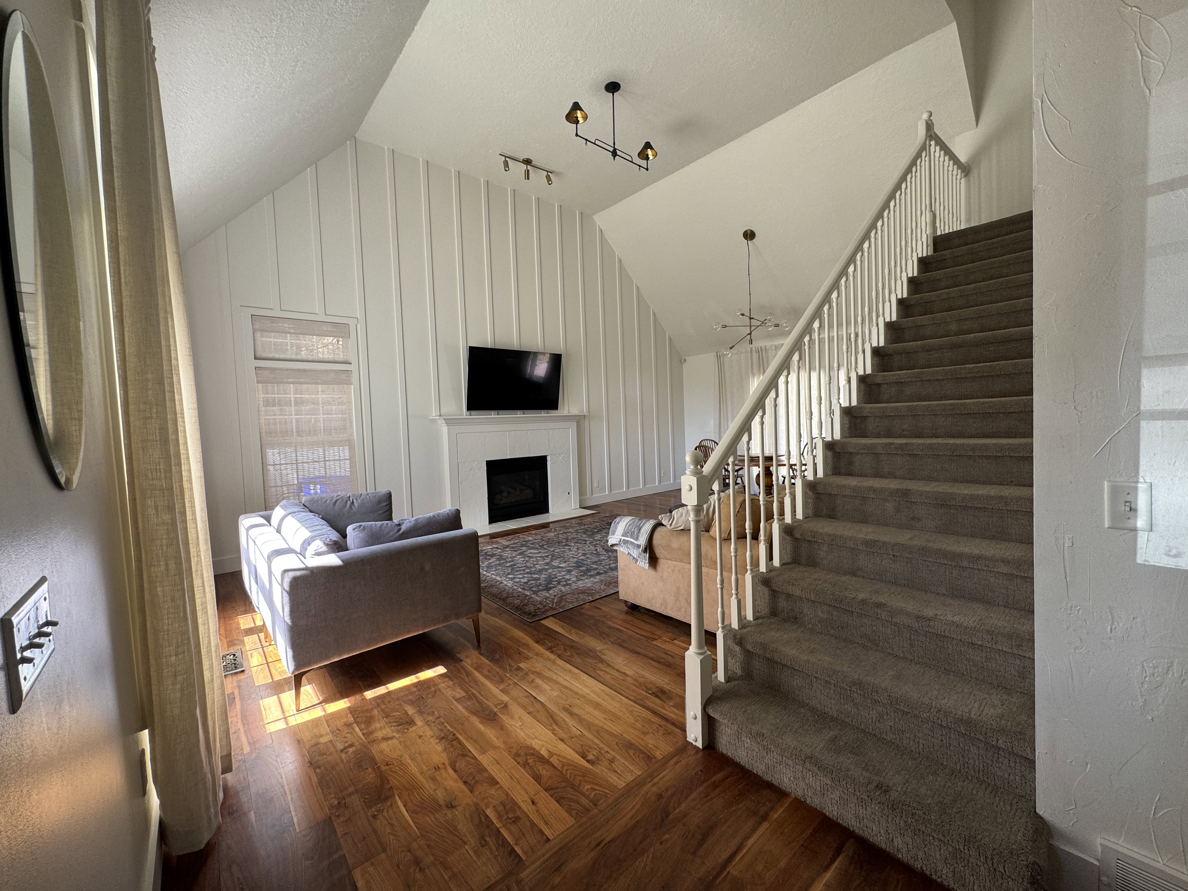Vaulted ceiling living area featuring wood-finish flooring, a white mantel fireplace, and vertical paneling accent wall